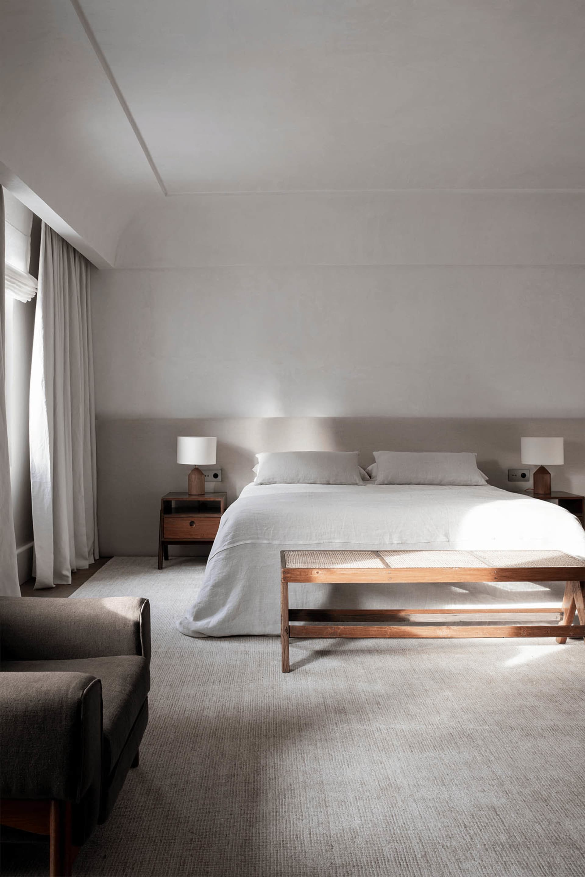 A minimalist bedroom featuring a large bed with linen bedding and wooden furniture.