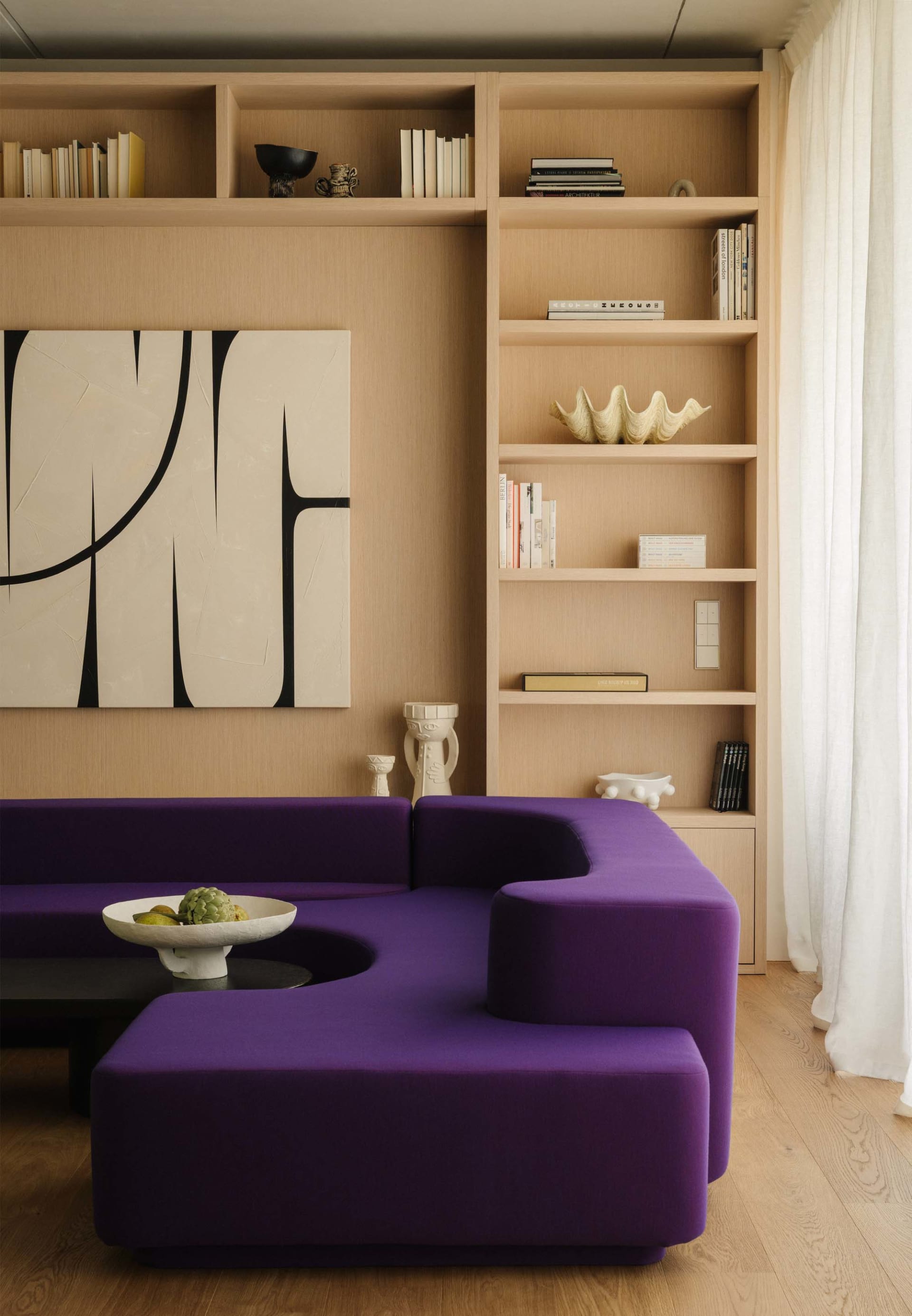 A modern living room featuring a purple sectional sofa and a built-in bookshelf filled with books and decorative items.