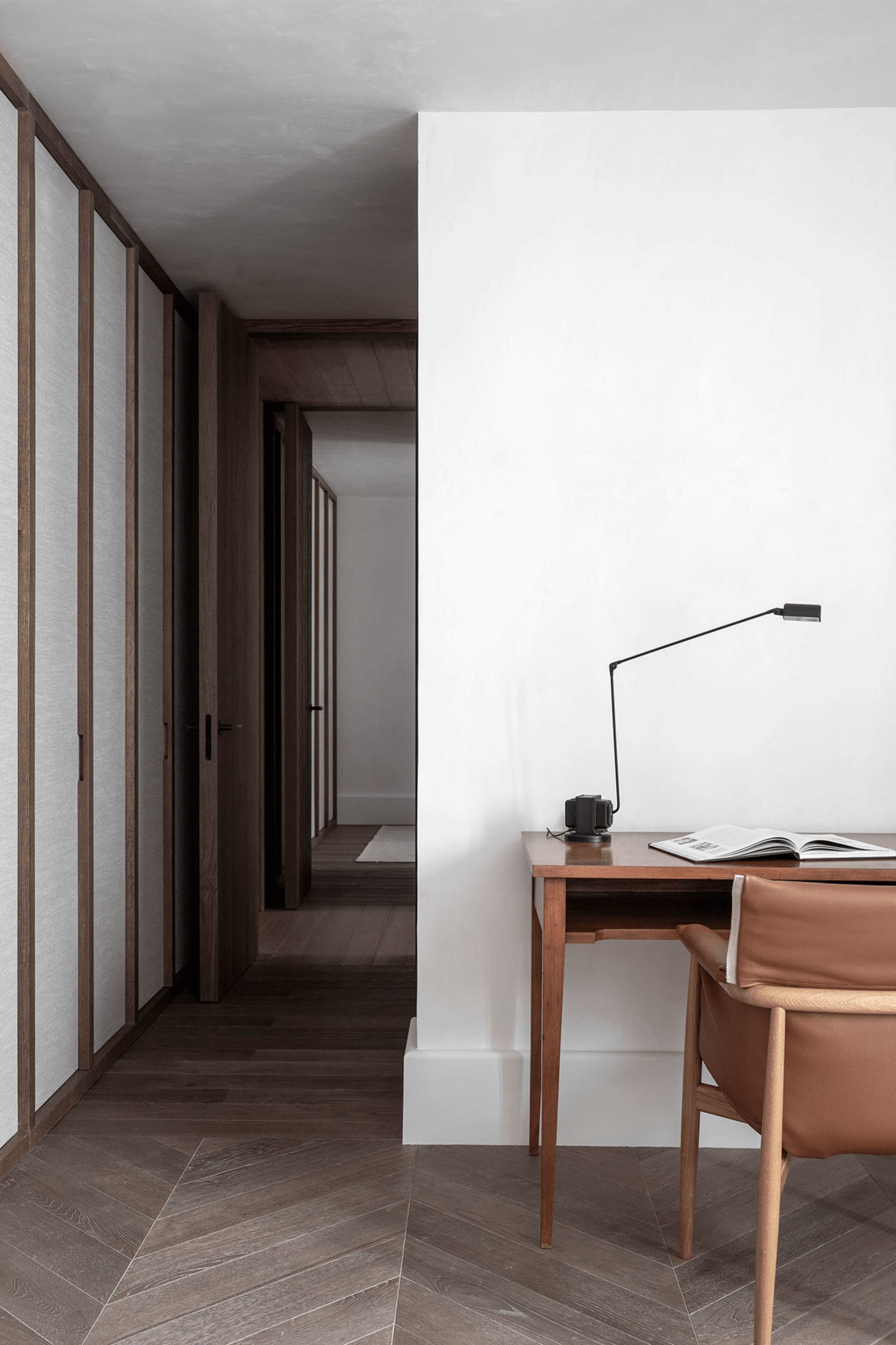 A minimalist home office with a wooden desk, leather chair, and metal desk lamp.