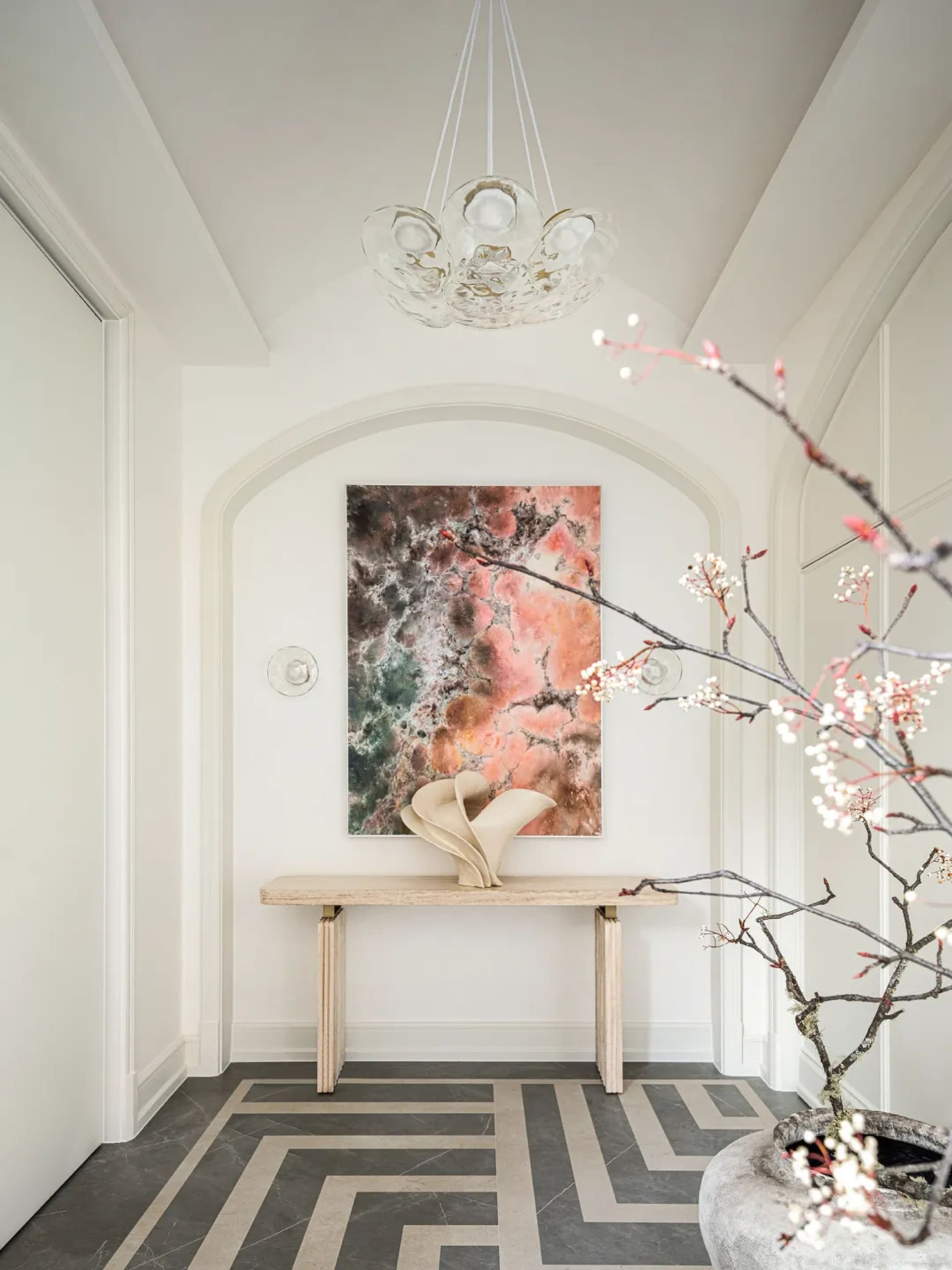 A modern entryway with a minimalist design, featuring a concrete floor and a table with a vase and abstract painting.