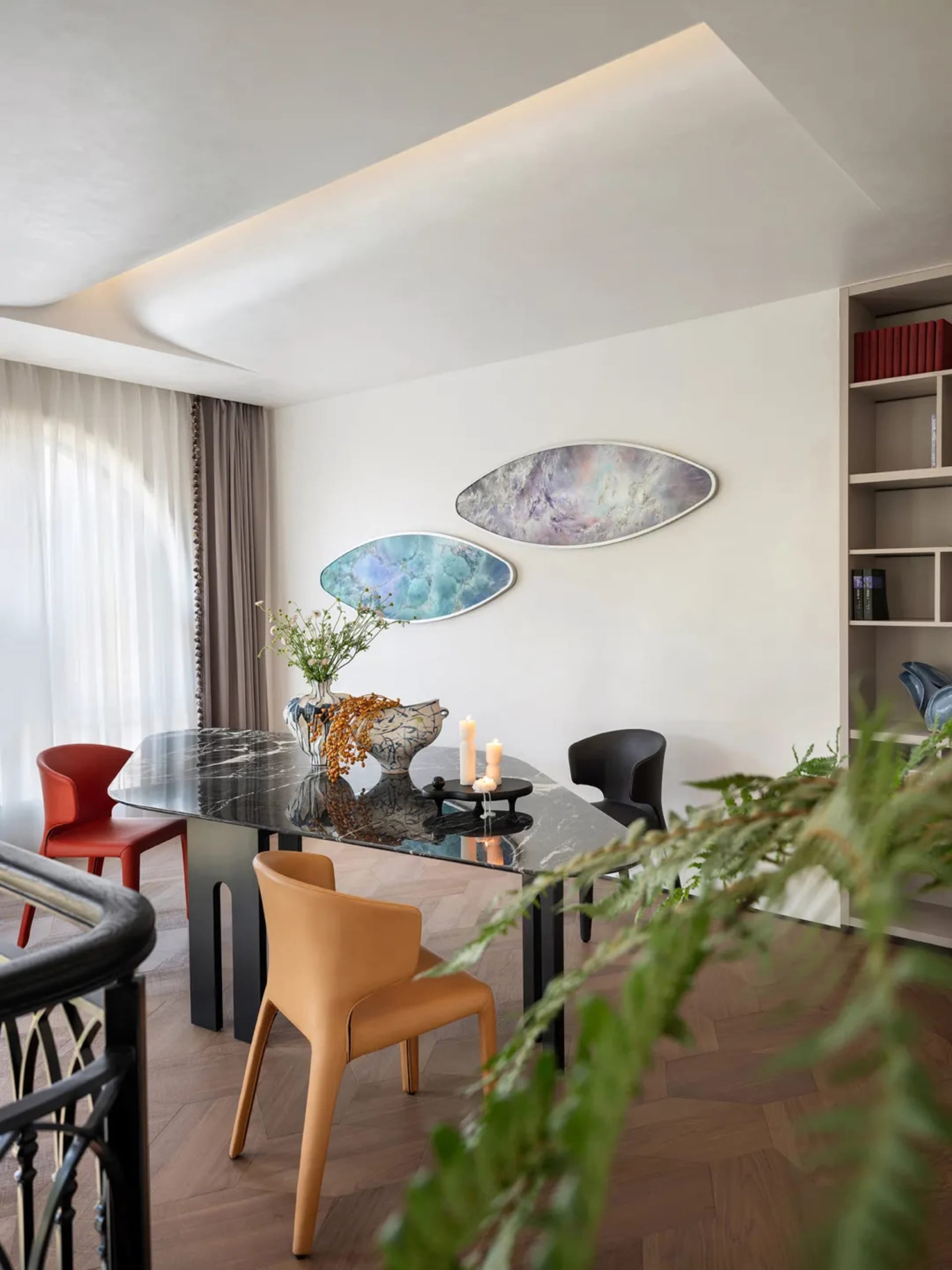A modern minimalist dining room with a metallic marble table, colorful chairs, and abstract wall art.