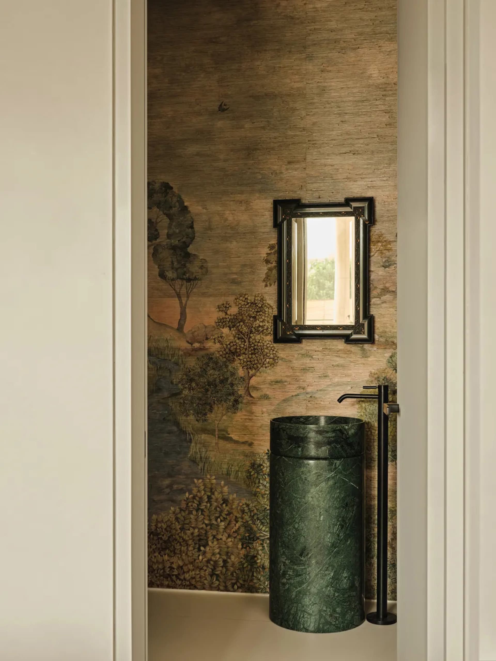 A traditional bathroom with marble walls, a green marble sink, and a framed mirror hanging above it.