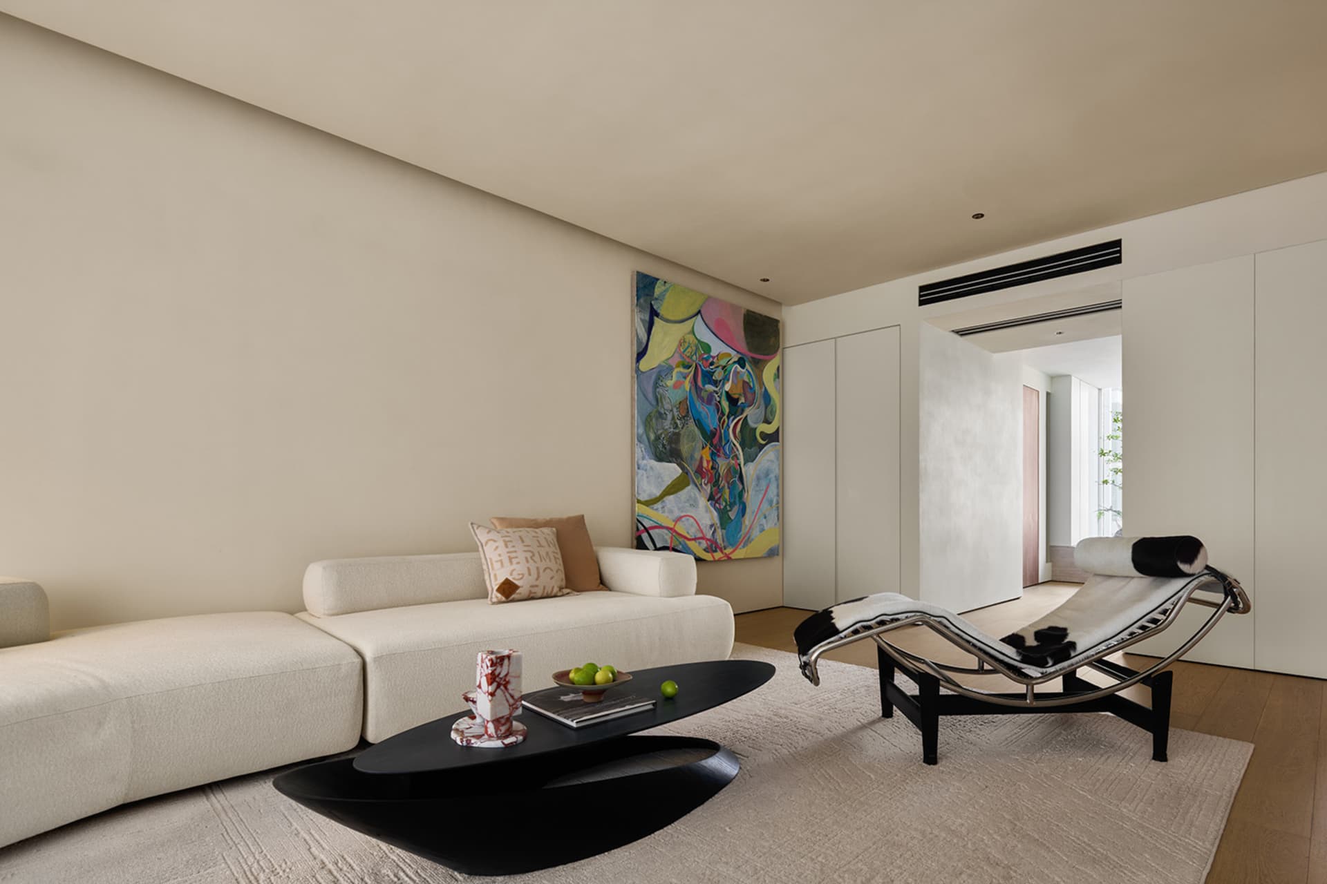A modern living room with a neutral-toned color palette featuring a white sofa, abstract painting, and black coffee table wit