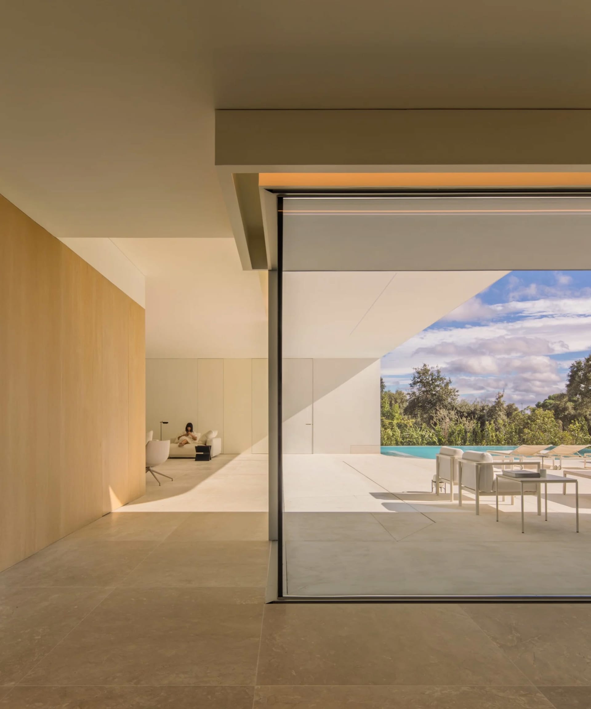 A modern minimalist living room with large windows and a view of the pool.