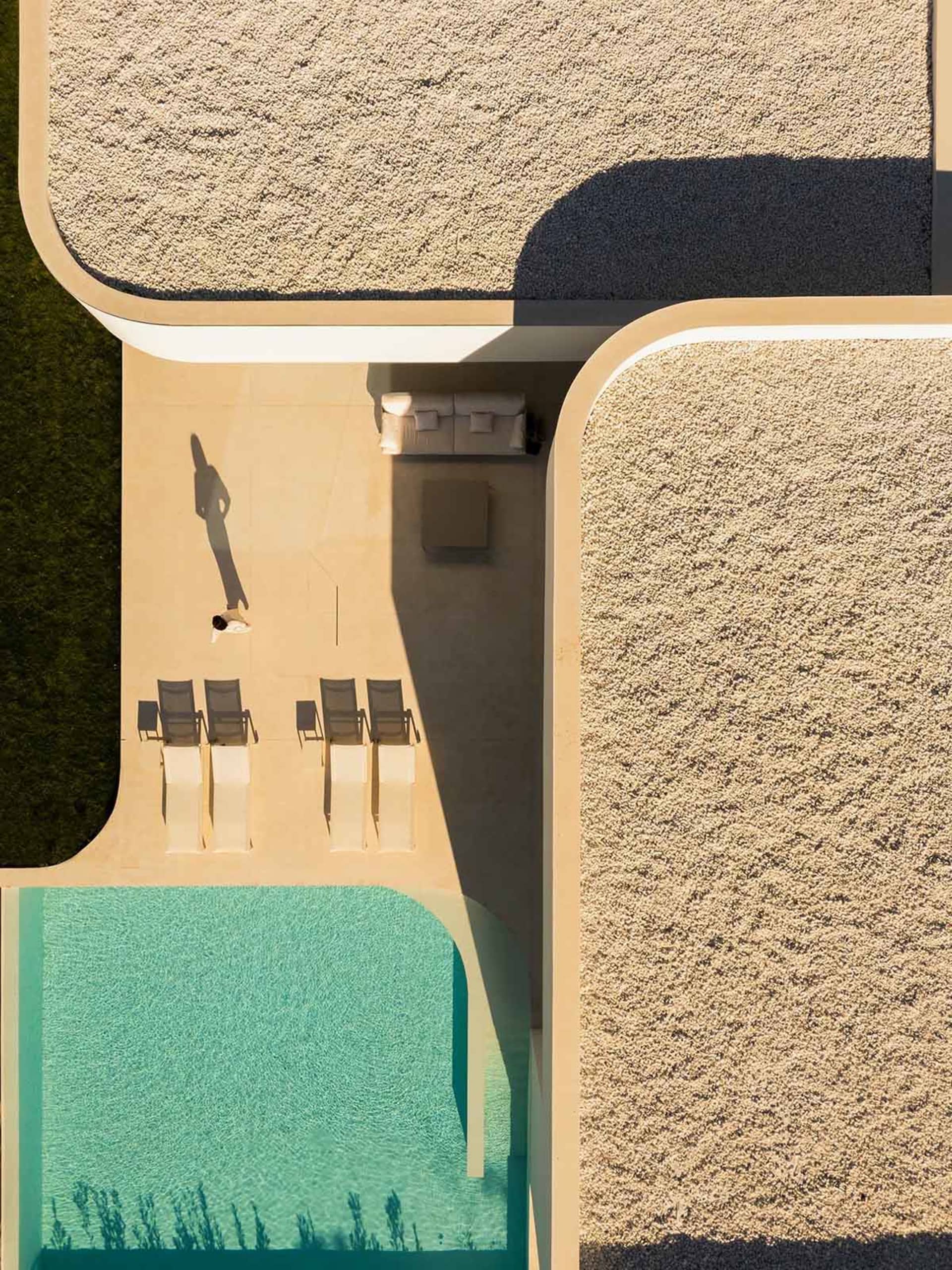 A modern minimalist patio area featuring a concrete floor and gravel accents, with a pool and outdoor seating.