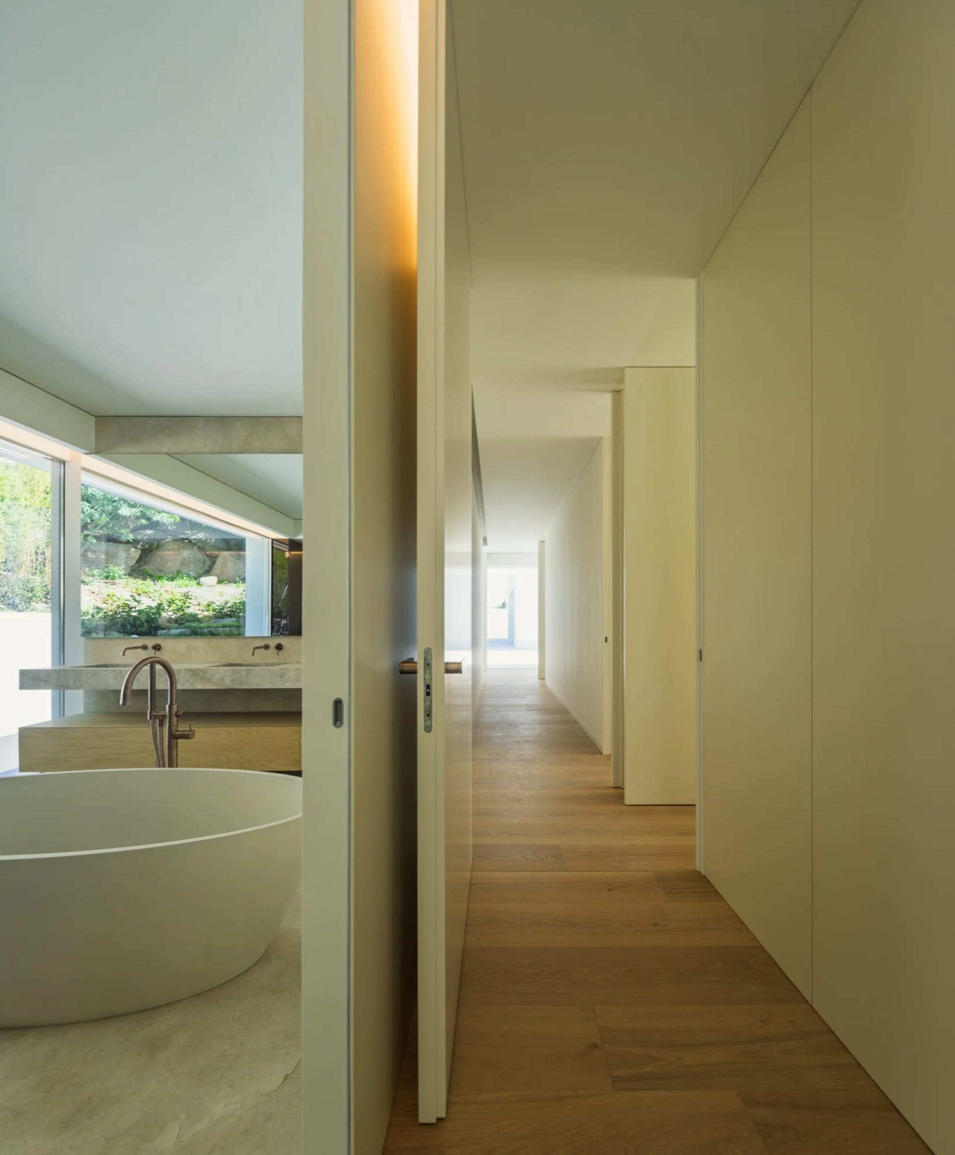 Modern minimalist bathroom with concrete walls, wood flooring, and a freestanding bathtub.