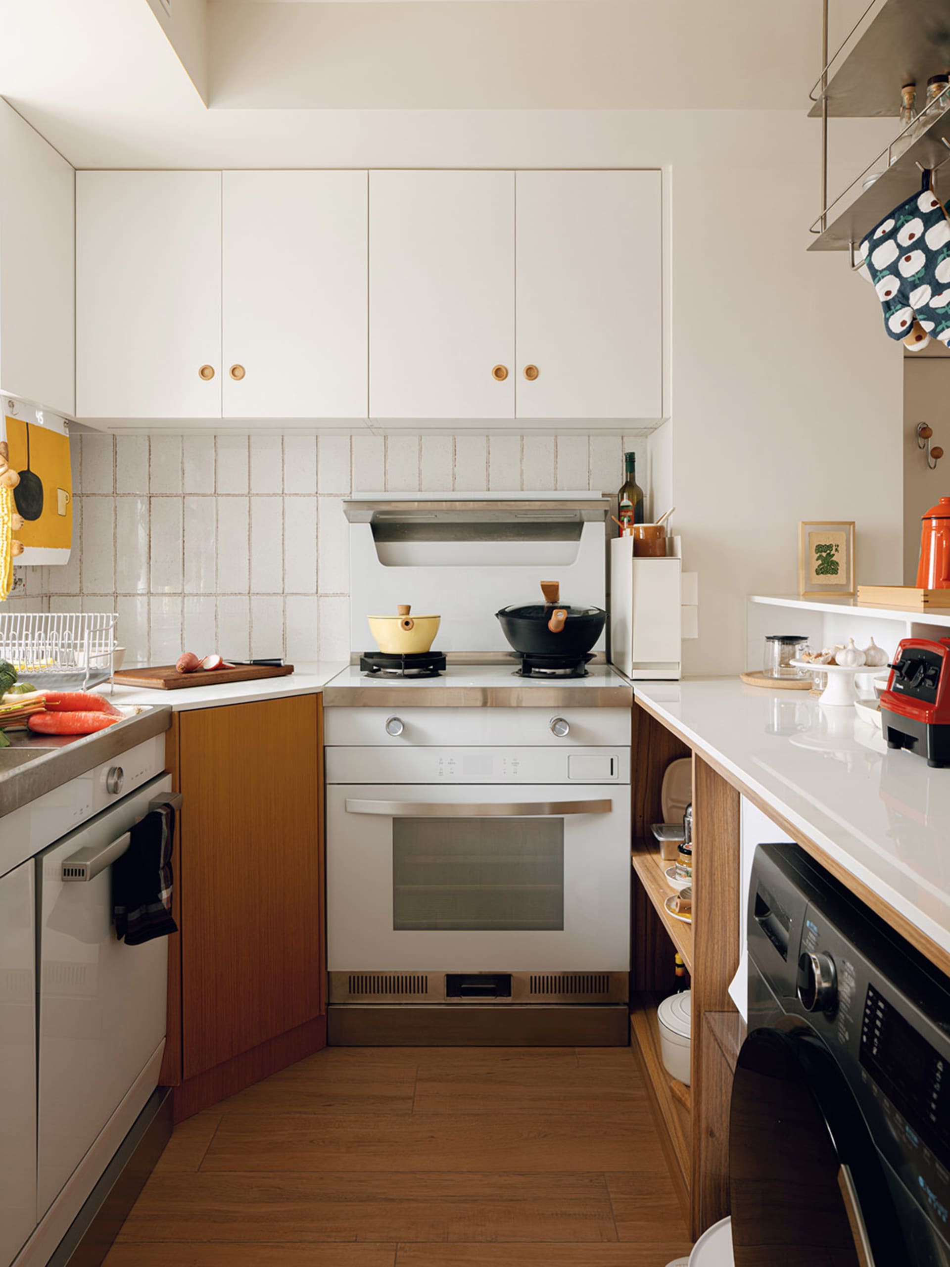 A modern, minimalist kitchen with white cabinets and a wooden floor.