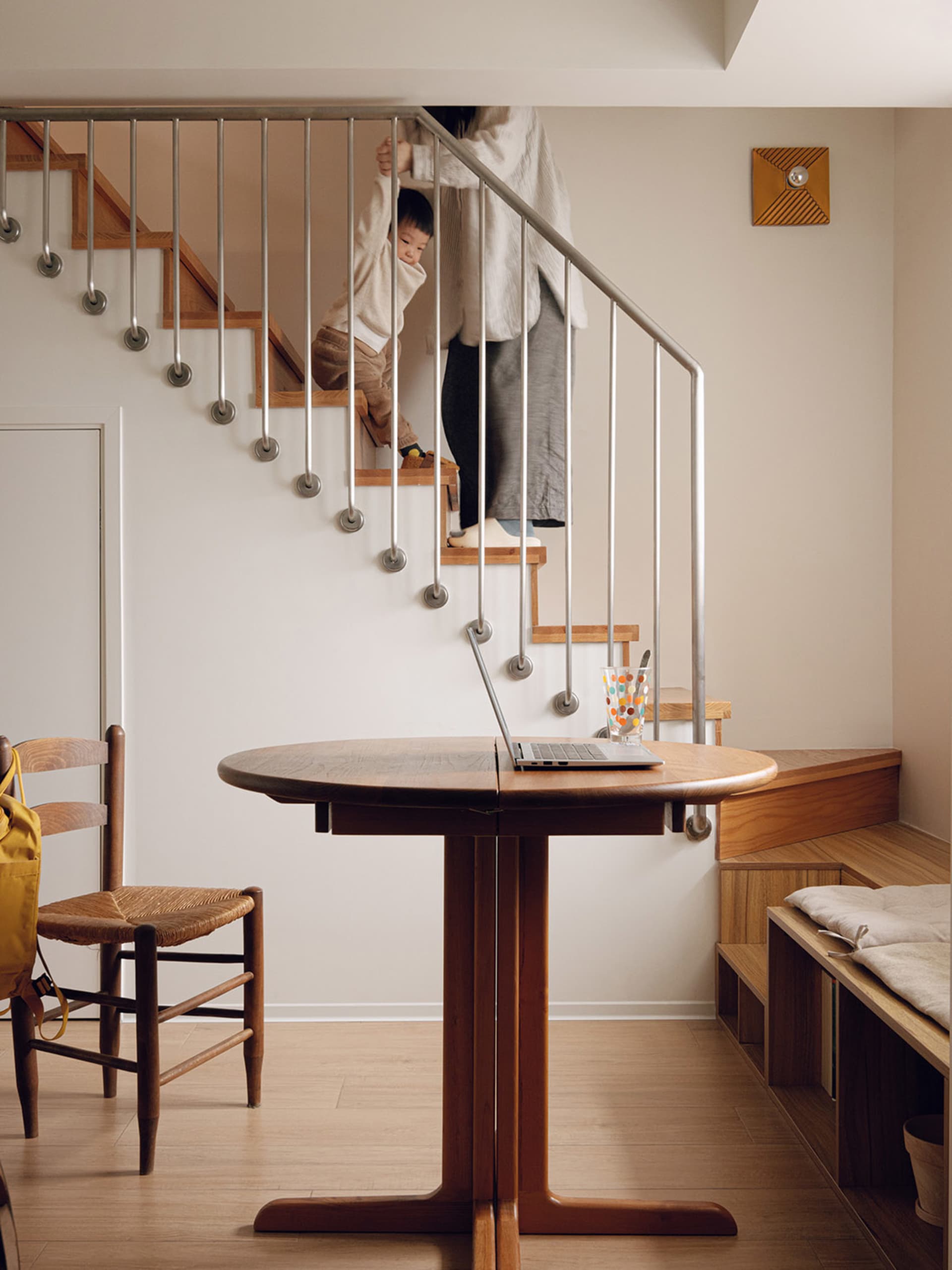 A modern home office featuring a wooden table, stairs, and a child climbing up the stairs.