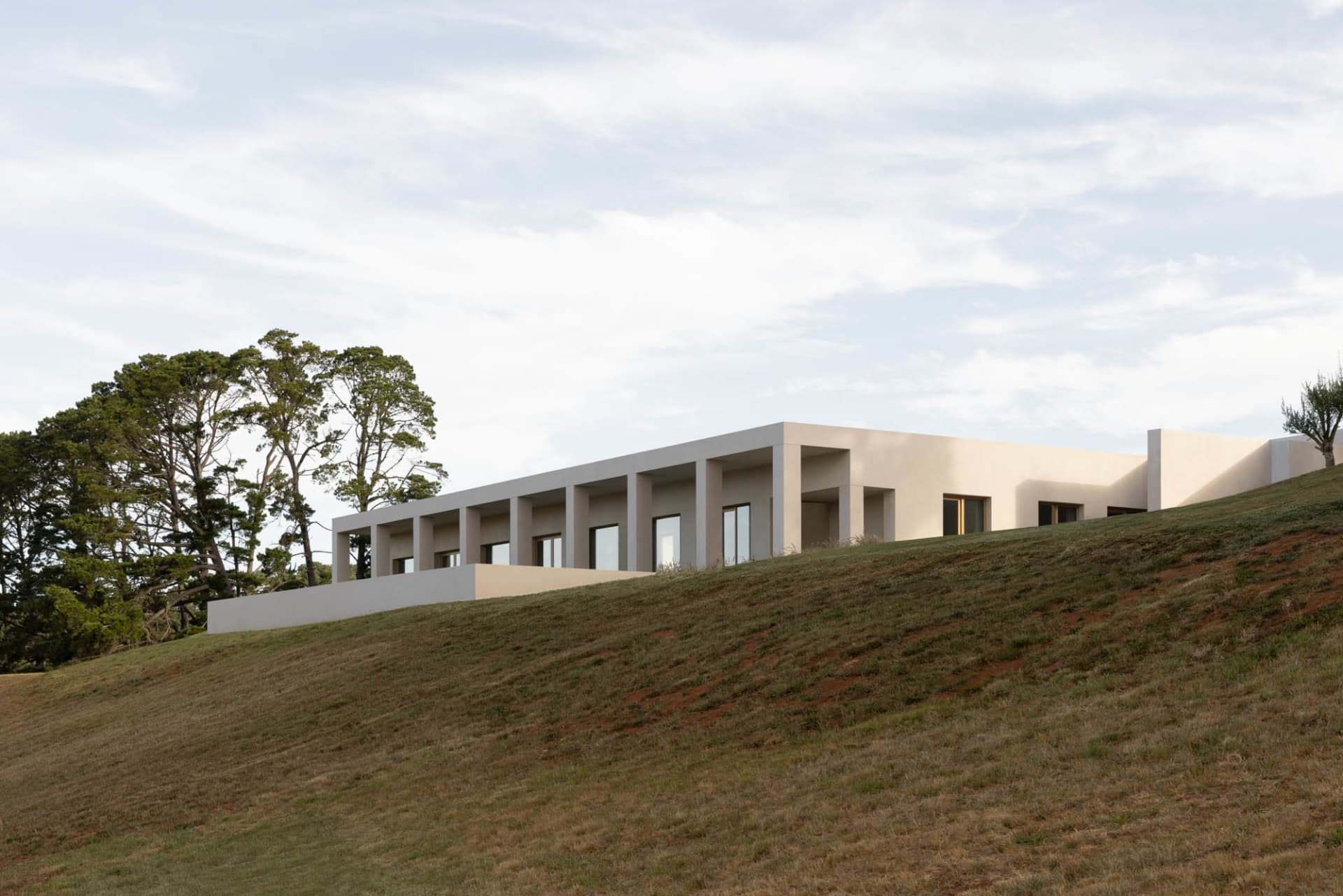 A modern house with a concrete exterior features large glass windows.