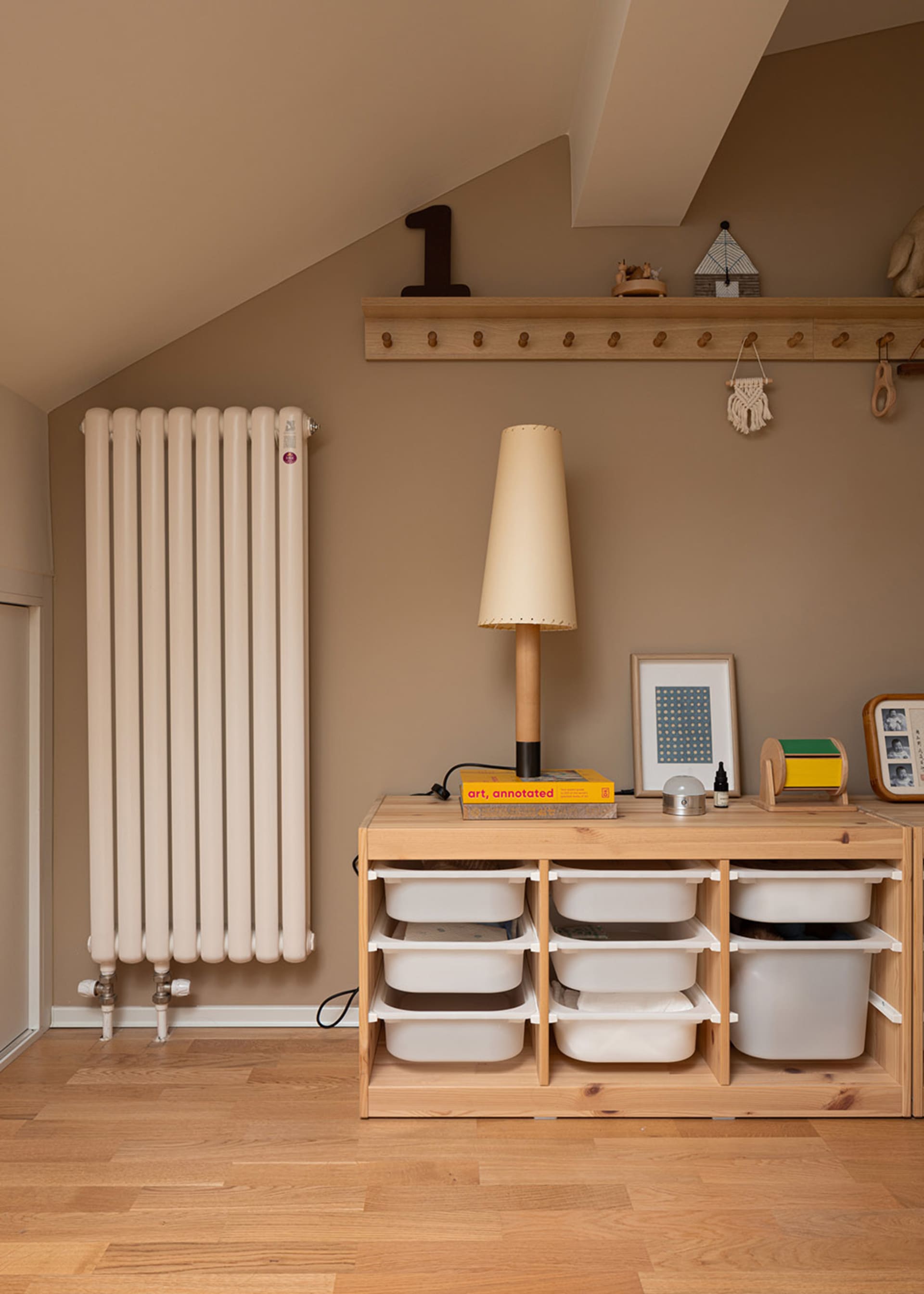 A modern interior design featuring a wood storage unit with white bins and a lamp on top, with a radiator and coat rack in th