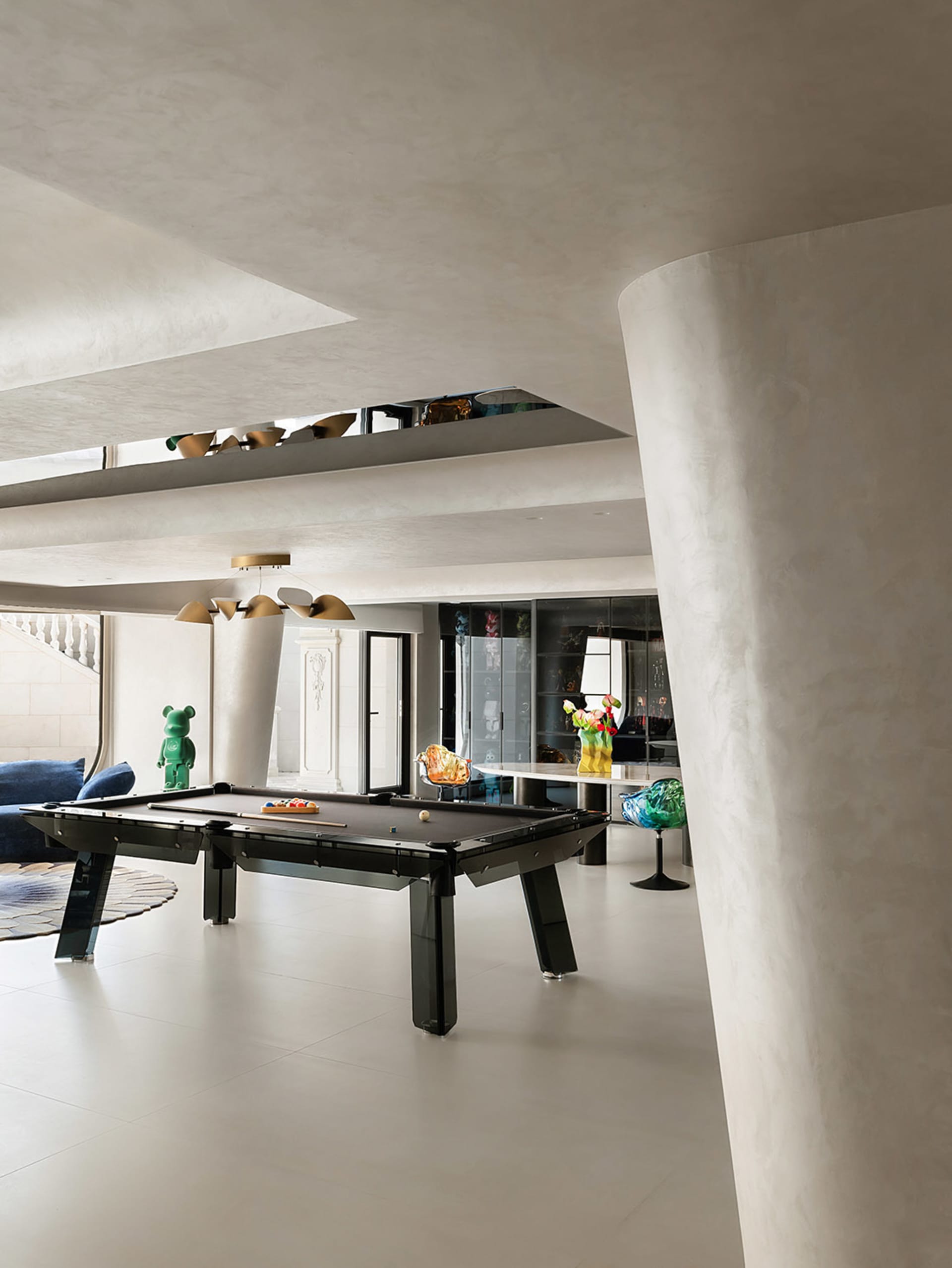 Modern living room with concrete walls and floor, featuring a sleek, black pool table and contemporary furnishings.