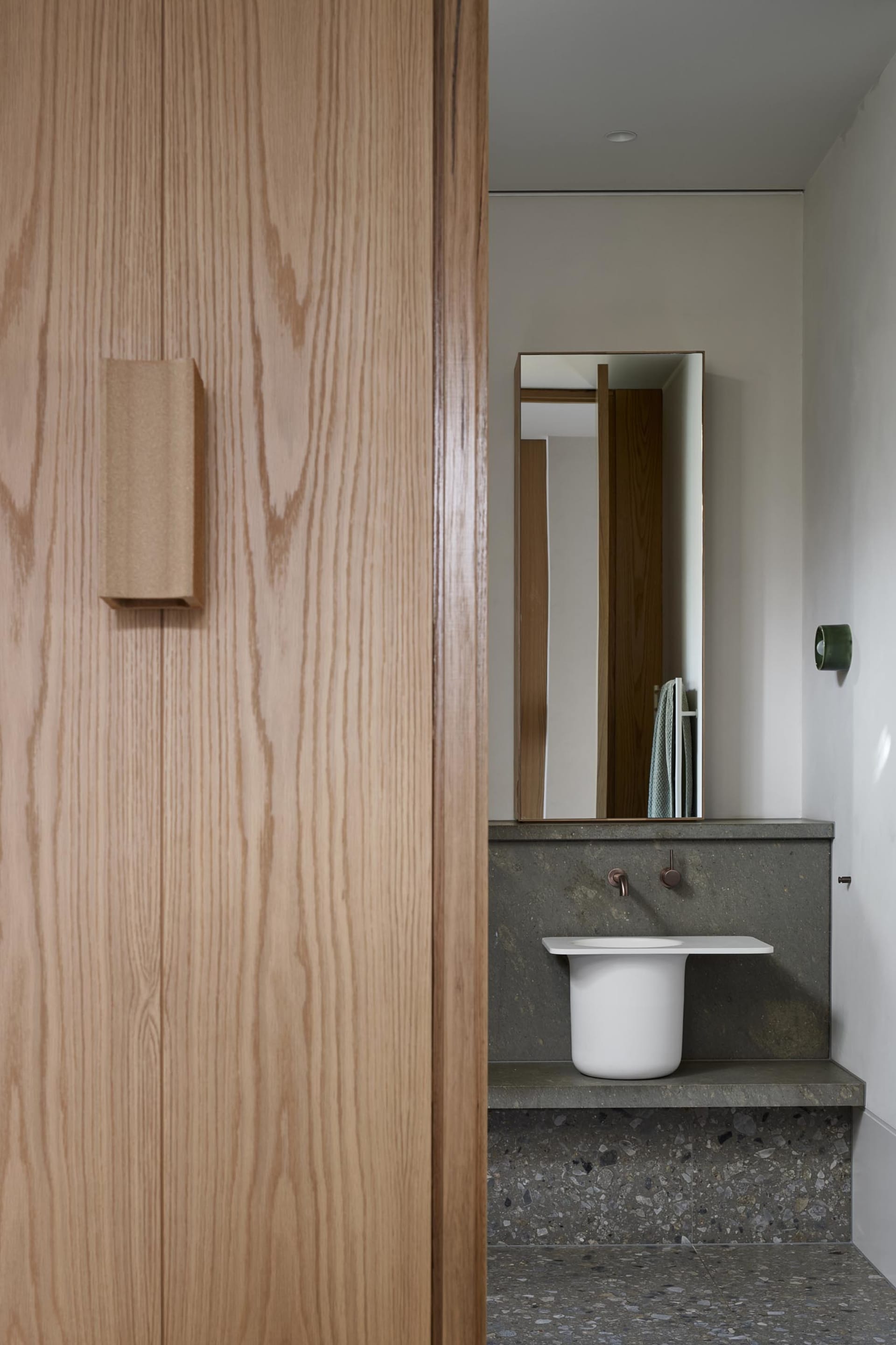 Modern minimalist bathroom featuring a sleek, white sink with a concrete countertop and a tall, rectangular mirror above it.