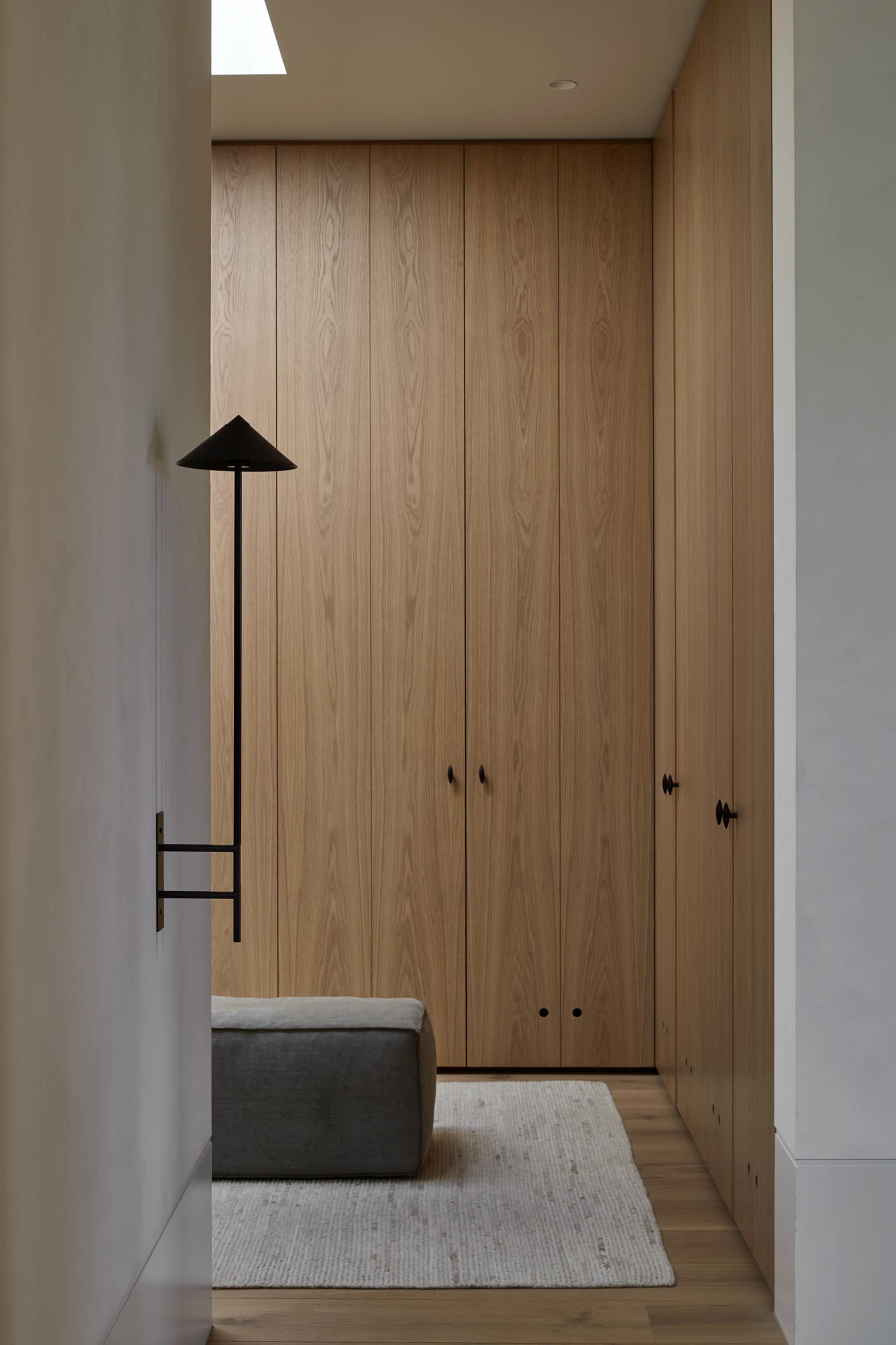 Modern minimalist closet with wood panels and a small ottoman on a white rug.