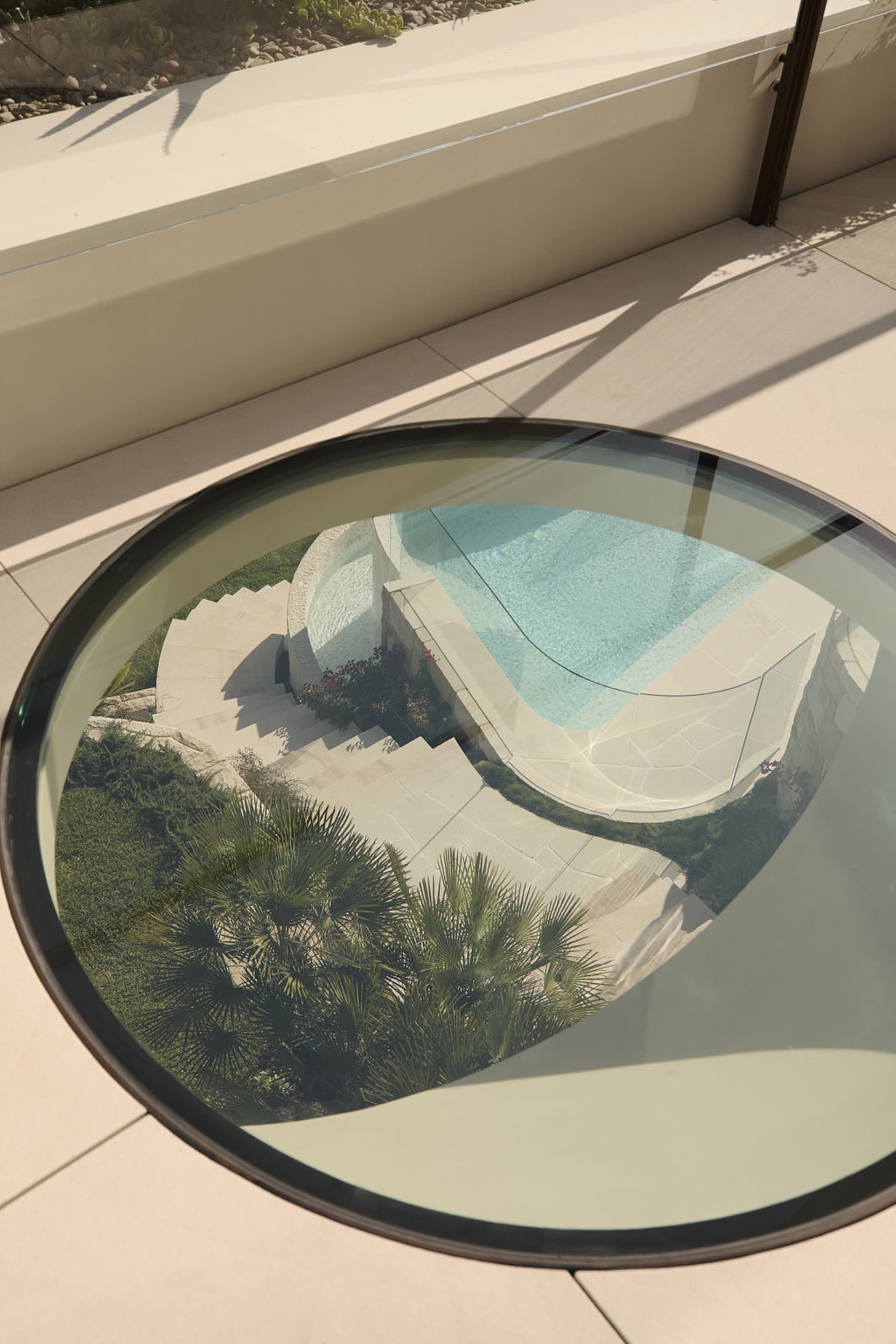 A modern outdoor space featuring a circular glass table with a view of a pool and steps.