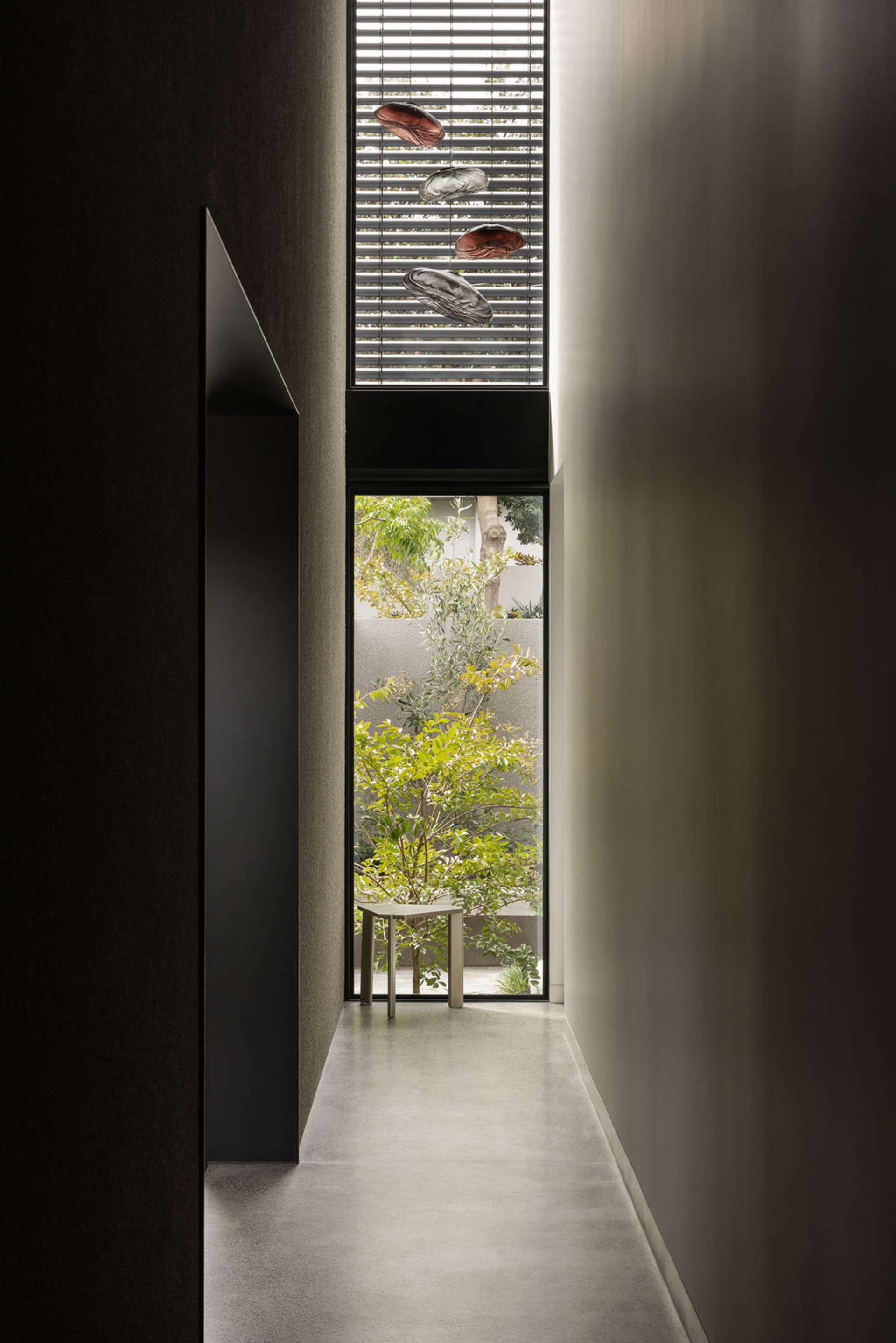 A modern residential interior with concrete walls, glass windows, and a view of a green courtyard.