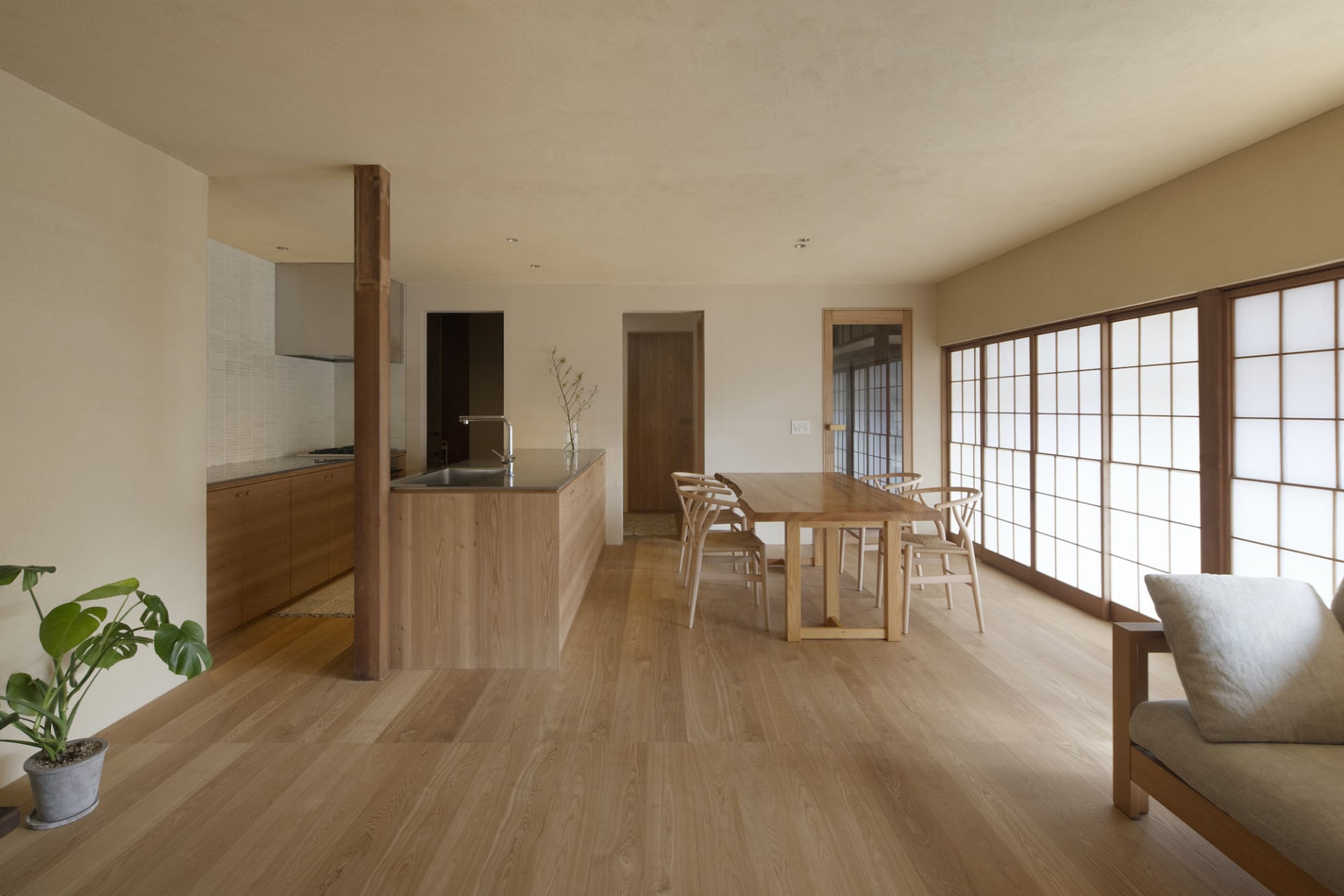 A modern, contemporary kitchen dining room with wooden furniture and cabinets, featuring a long wooden dining table with chai