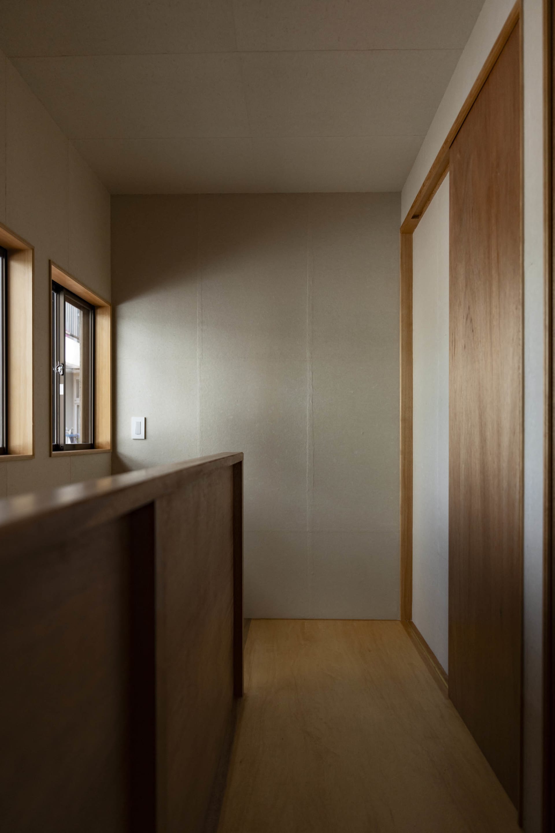 A modern corridor with wooden paneling and a minimalist design, featuring a light switch and a small window.