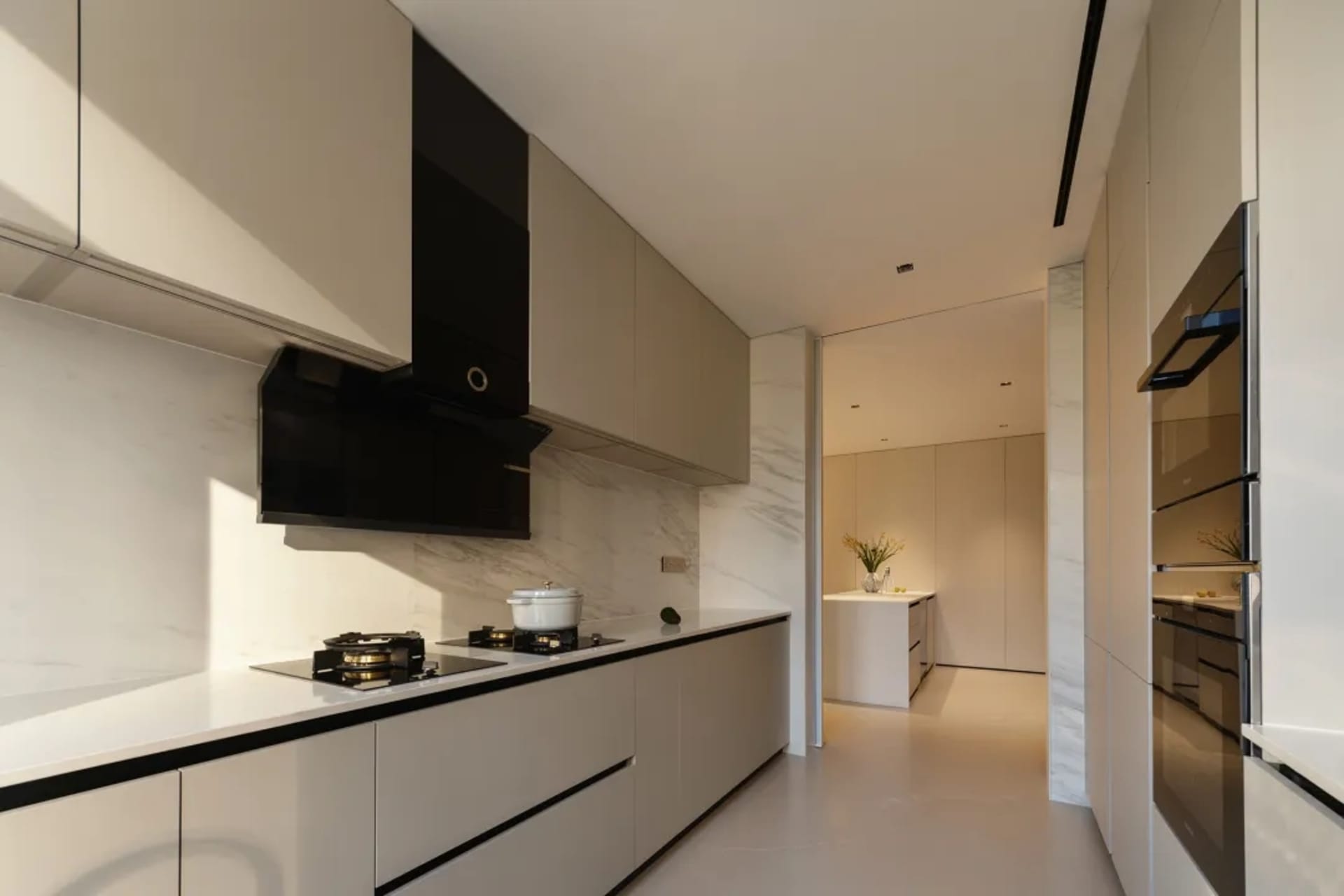 Modern minimalist kitchen with white marble countertops and cabinets, black appliances, and a white marble backsplash.