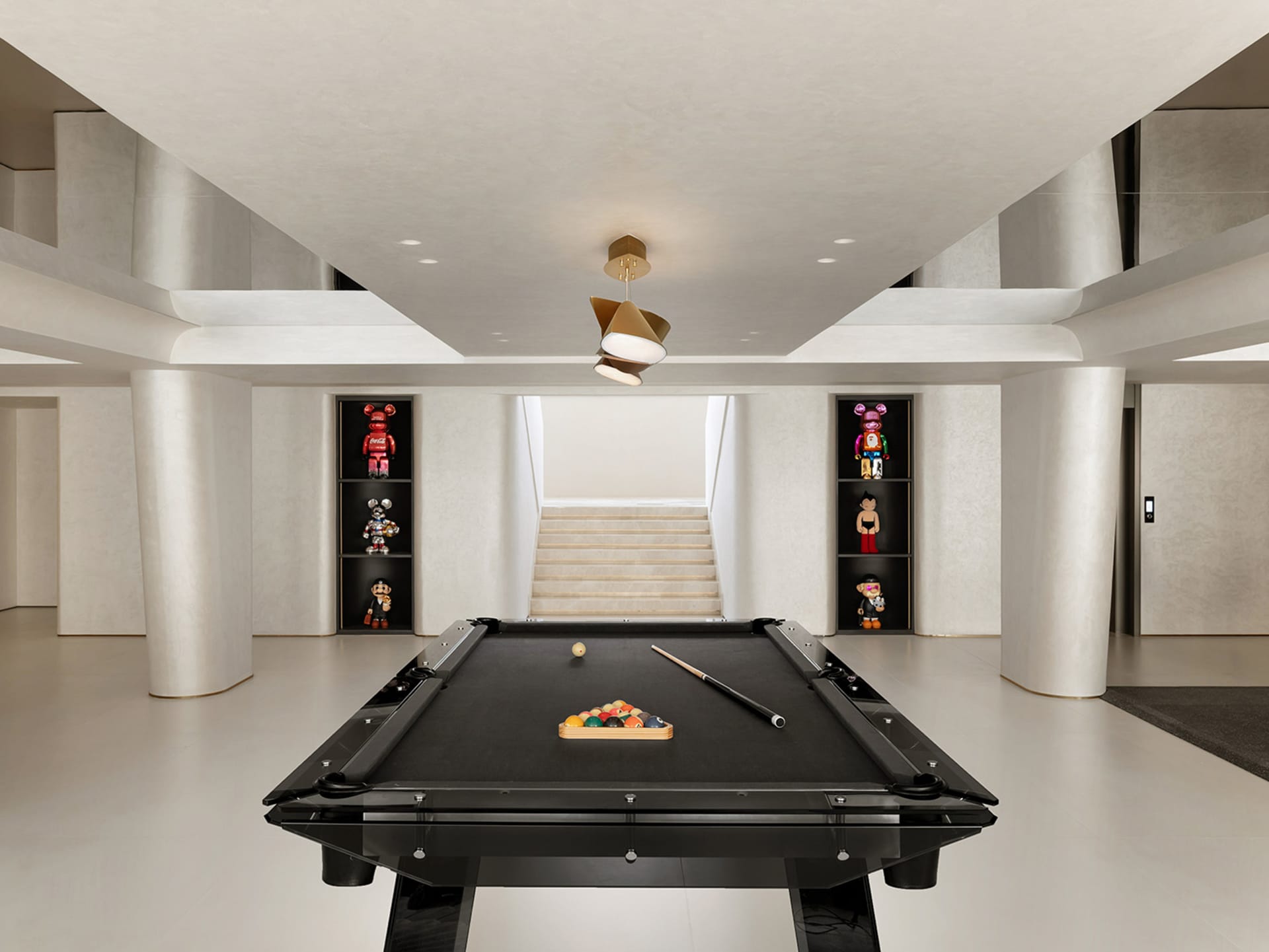 A minimalist playroom featuring a black pool table with billiard balls and cues, surrounded by concrete pillars and shelves d