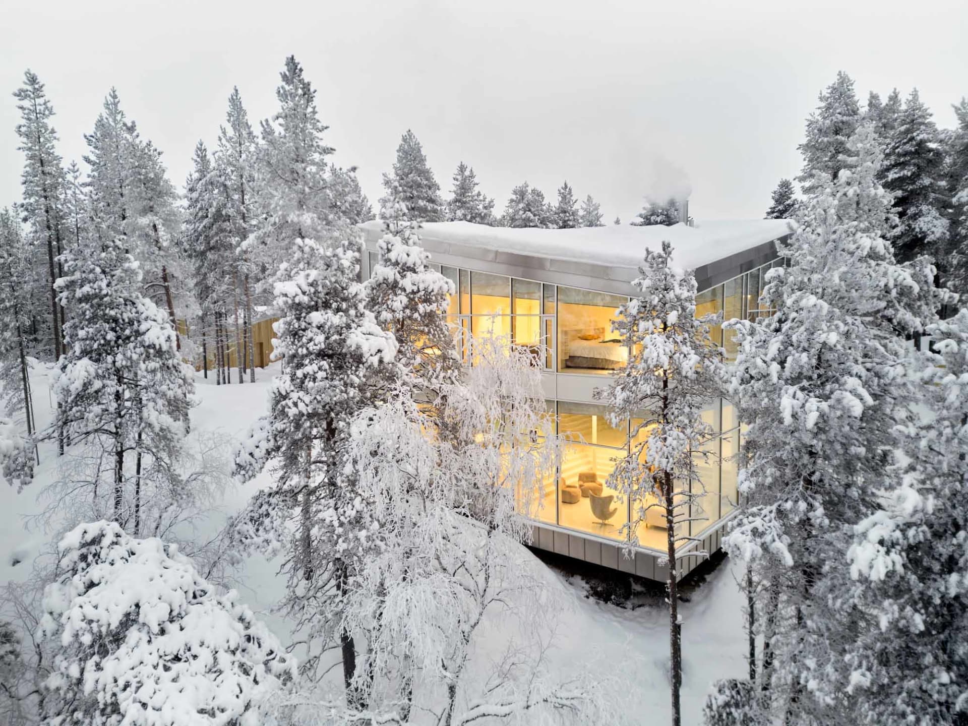 Modern glass house nestled in a snowy winter landscape.