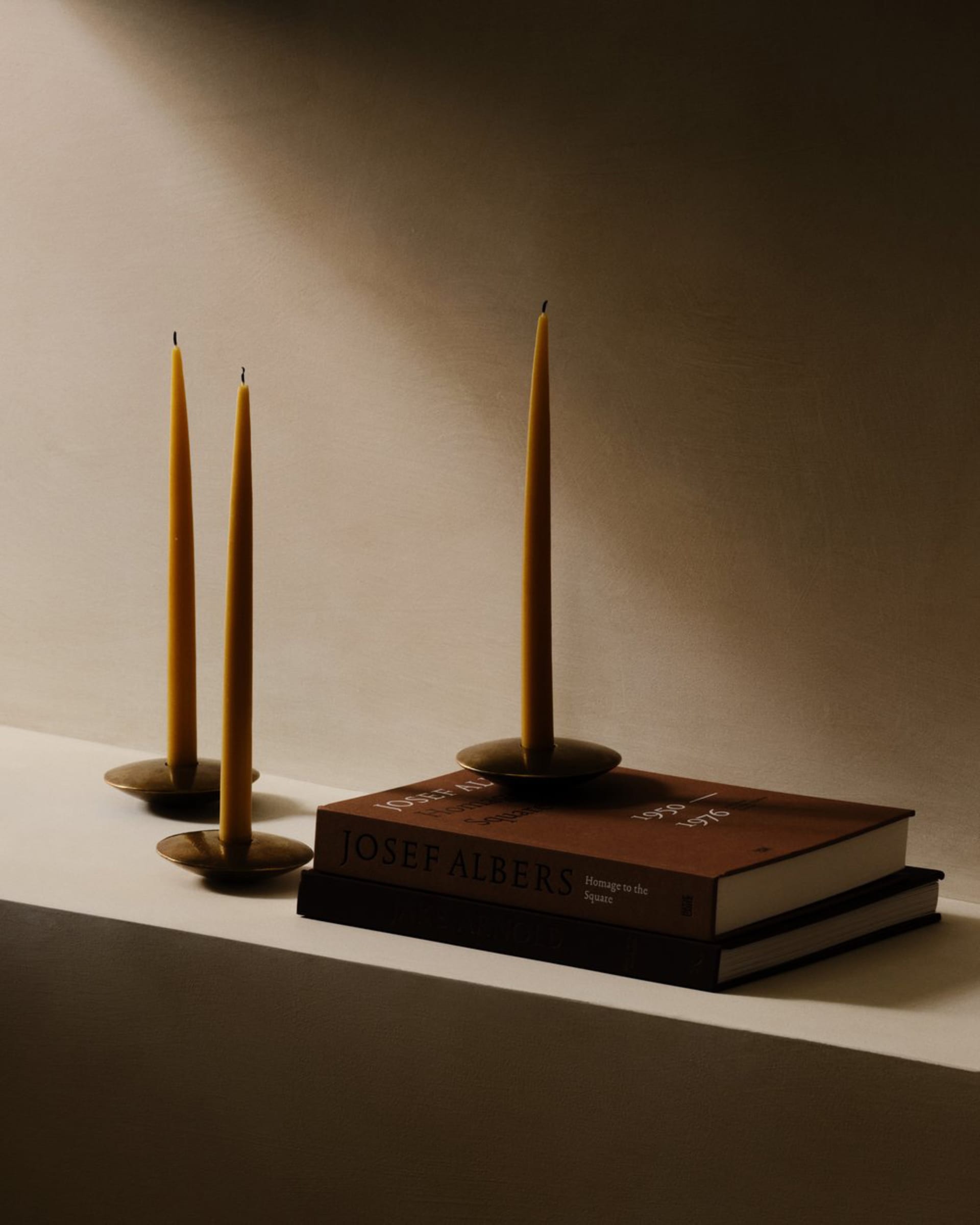 Two candles on brass candle holders and two books on a shelf with a soft lighting effect.