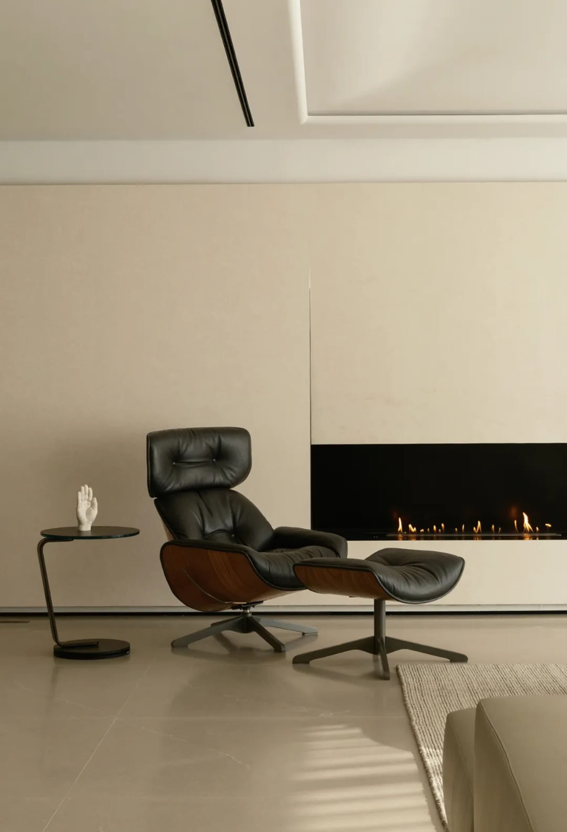 A minimalist living room featuring a black leather and wood armchair with a footstool, a side table with a sculpture, and a m