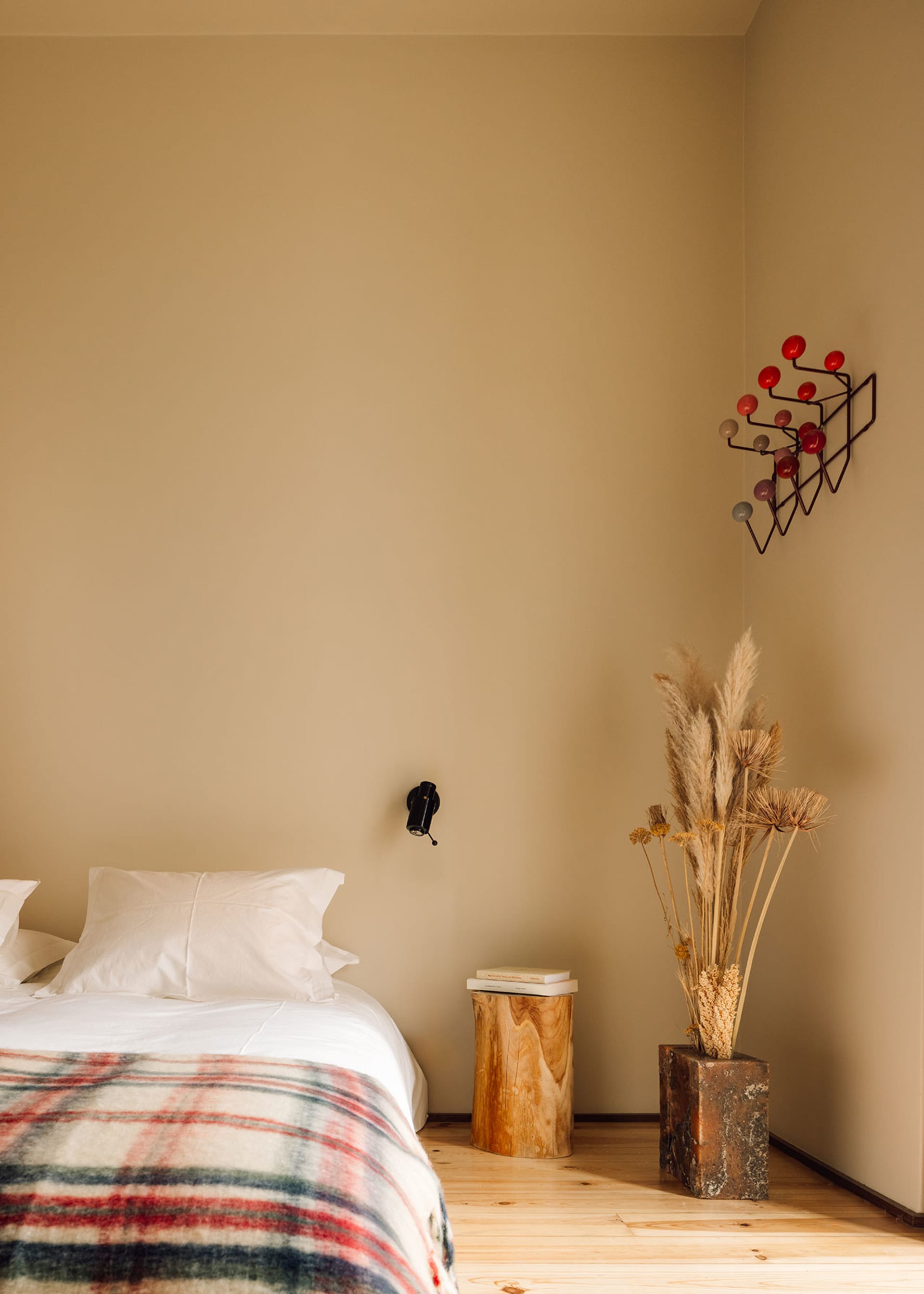 A minimalist bedroom with brown walls, a wooden bed frame, and a wooden side table with dried plants and a vase.