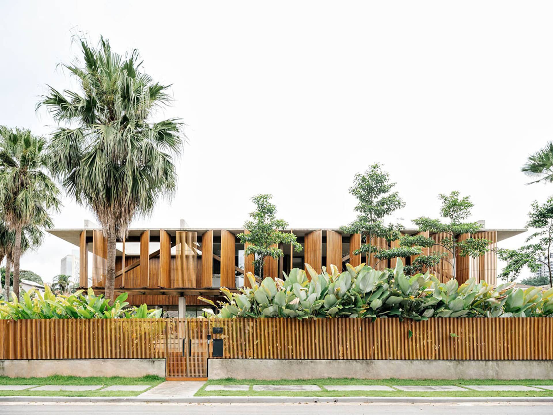 Modern residential house with wooden exterior, surrounded by plants and palm trees.