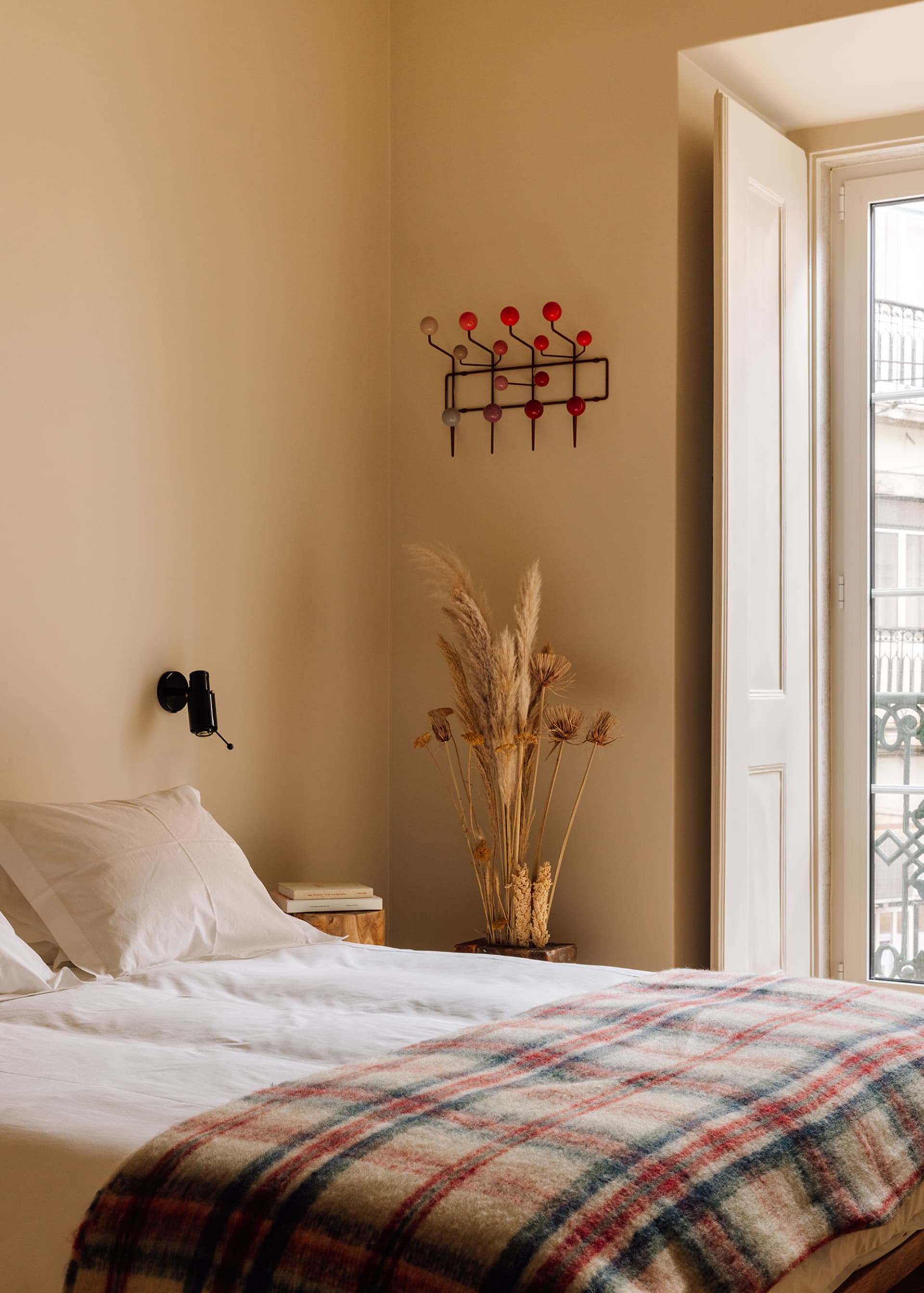 A minimalist bedroom with a bed, pillows, a checkered blanket, and a decorative plant in a vase.