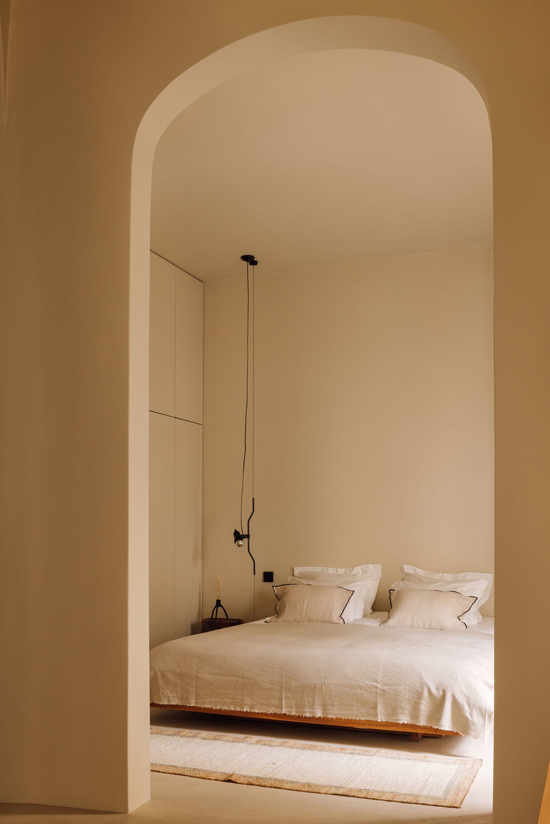 A minimalist bedroom with a white bed covered in soft textiles and wooden flooring.