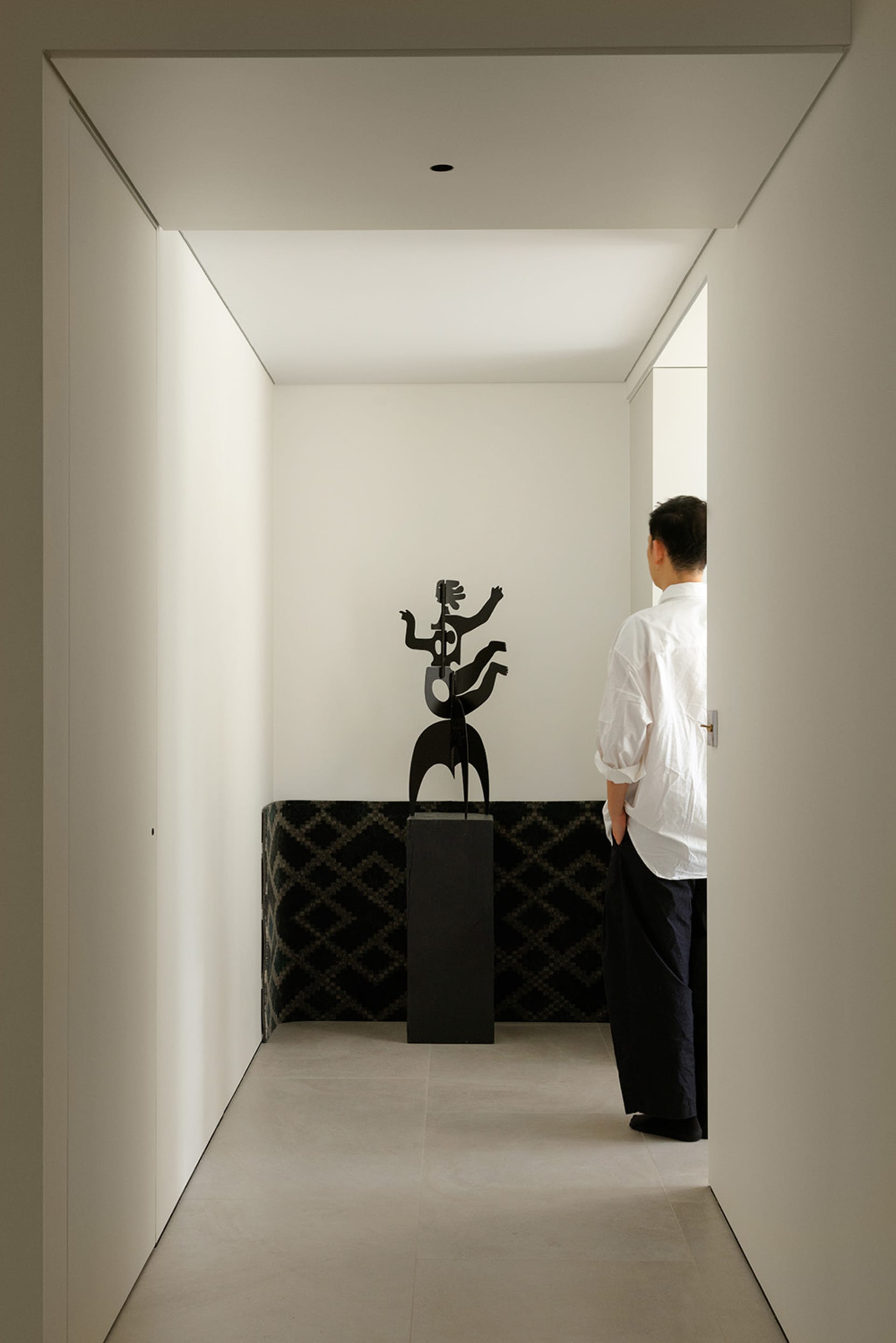 A black metal sculpture positioned in a minimalist white entryway.