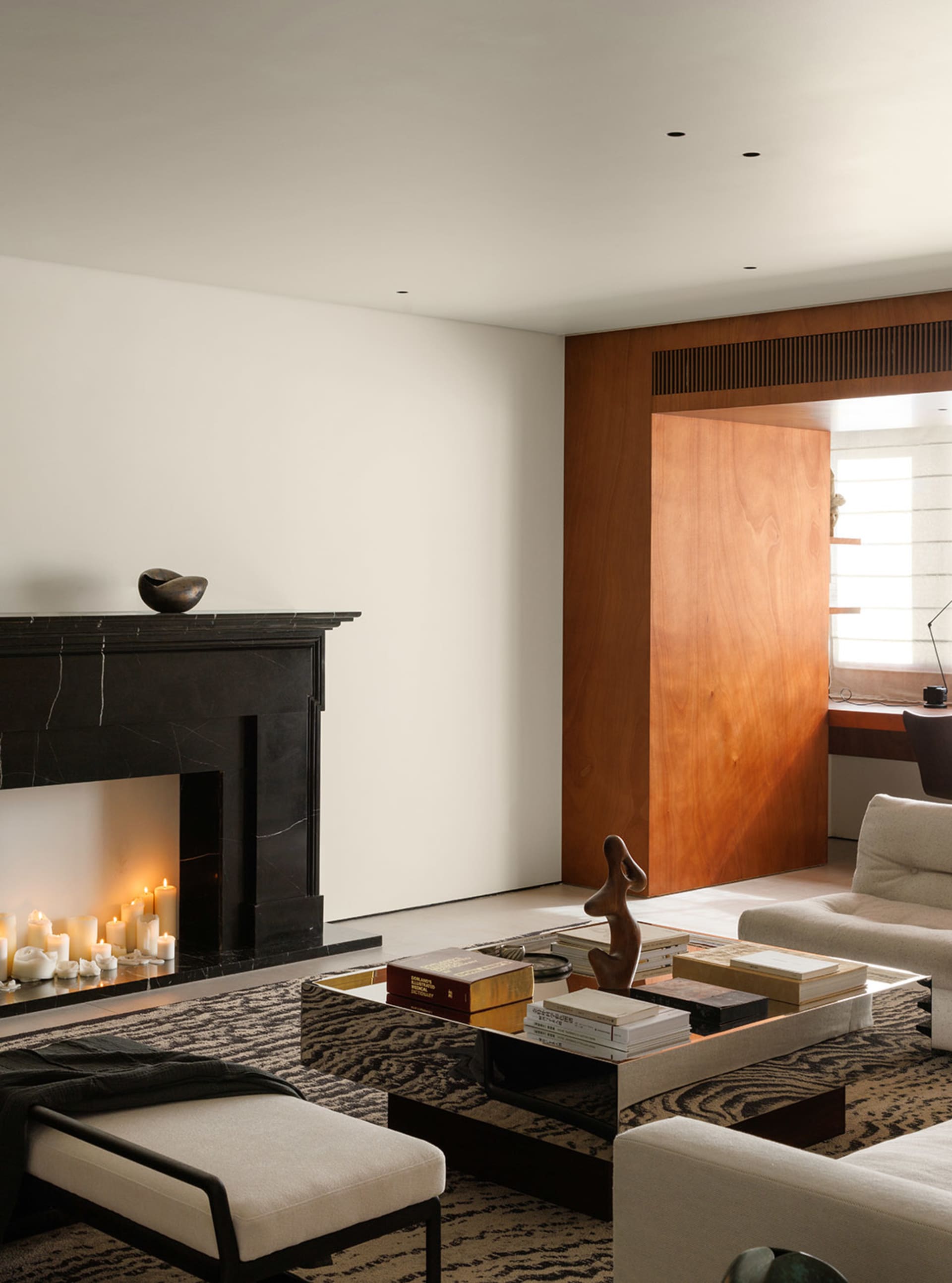 A modern living room with a black marble fireplace, a wooden accent wall, a white coffee table with books and a sculpture, an