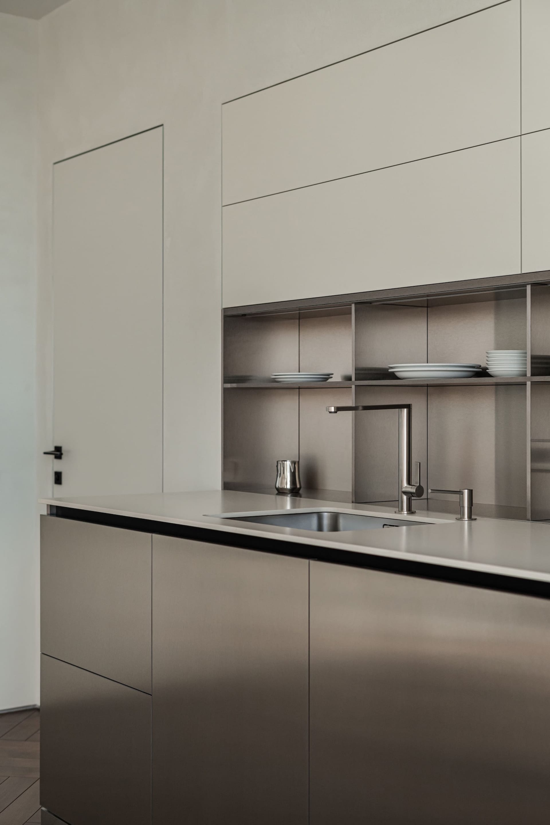 Modern minimalist kitchen with stainless steel cabinets and countertops. Open shelving and sleek design.