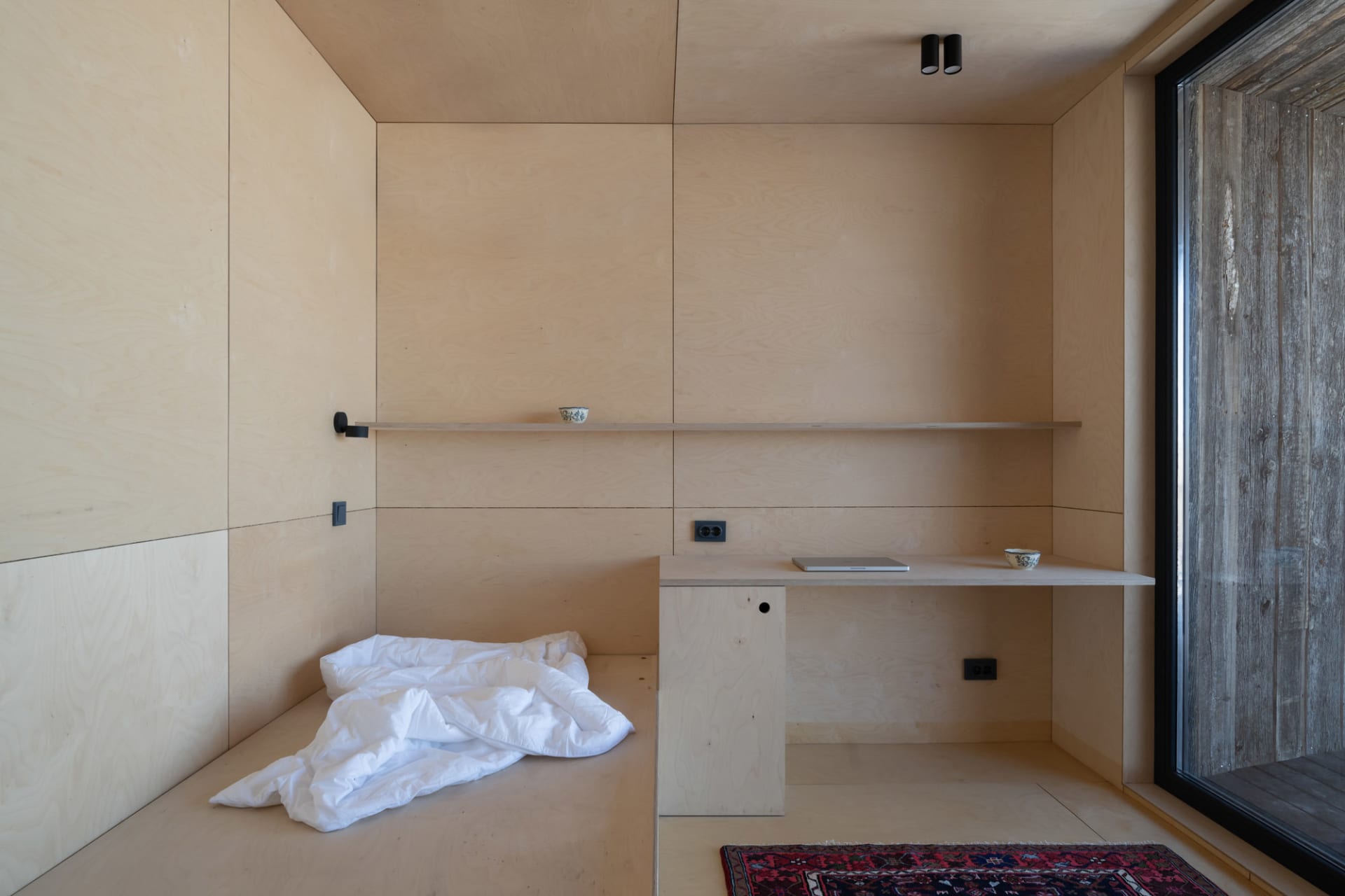 A minimalist living room with wooden walls, shelves, and a desk.