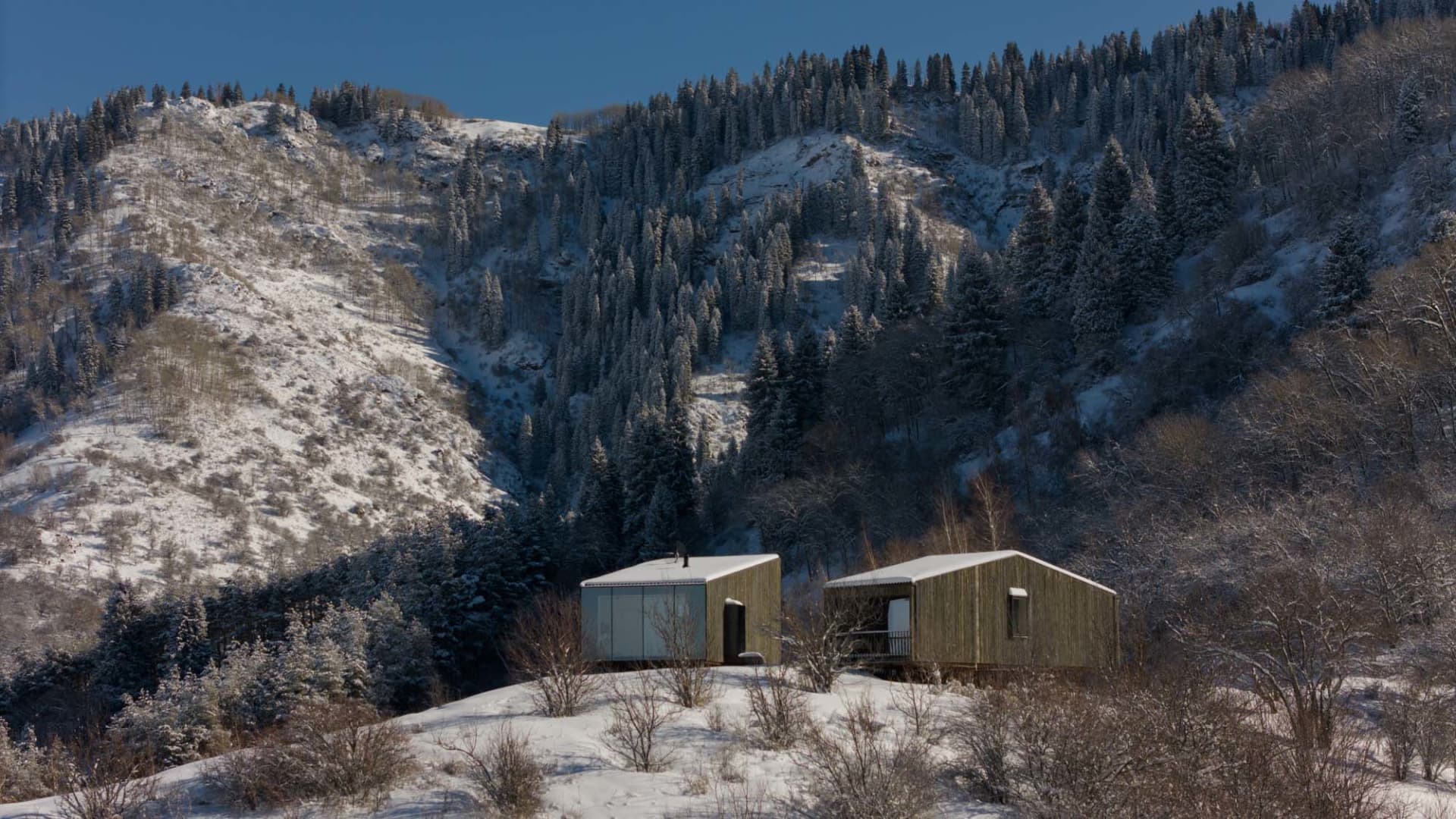 一棟擁有木質外觀的現代住宅,靜靜坐落在覆雪的山坡上。