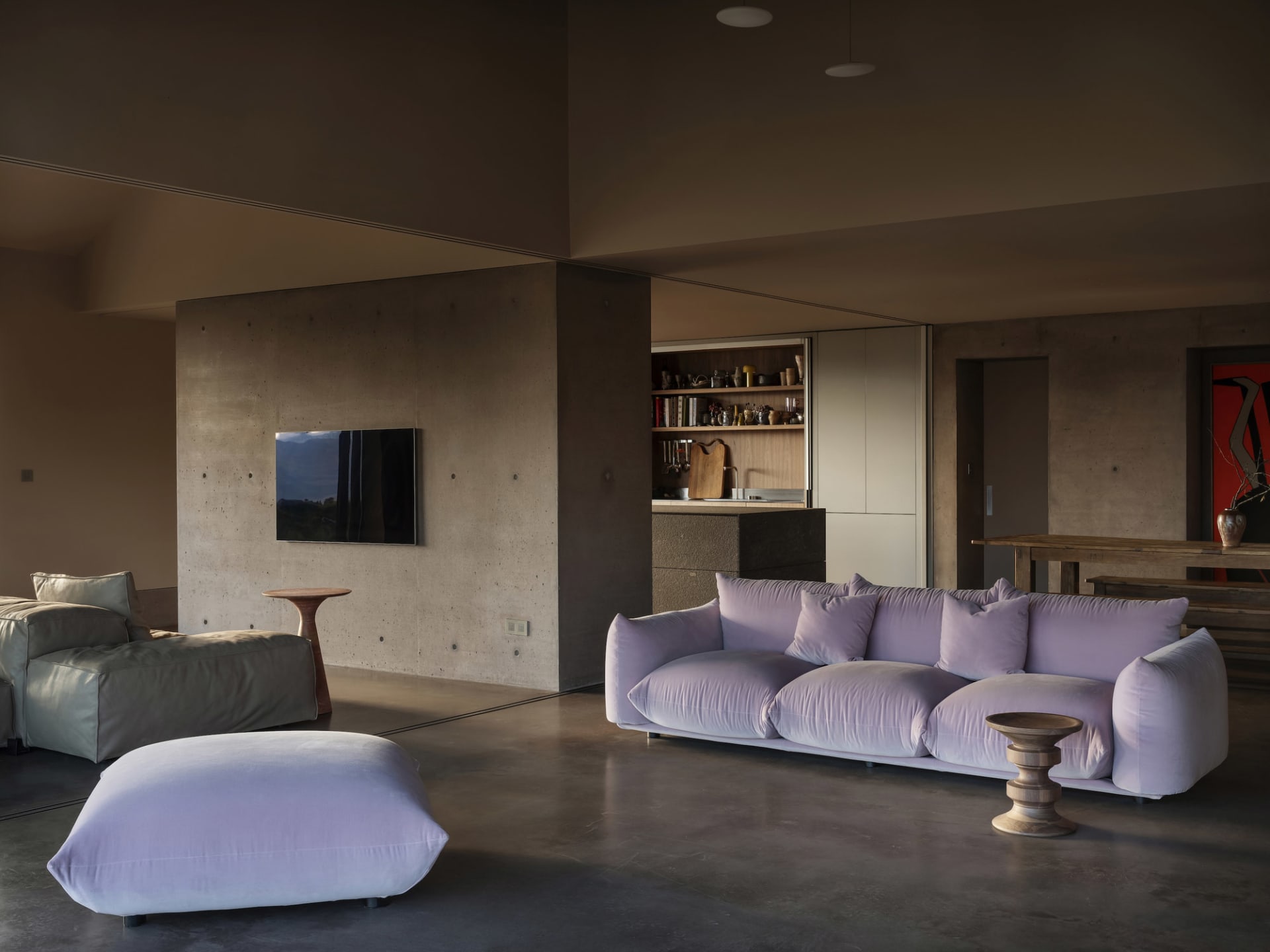 A modern interior space with a concrete floor, featuring a cozy purple sofa, a minimalist living area, and a glimpse into the