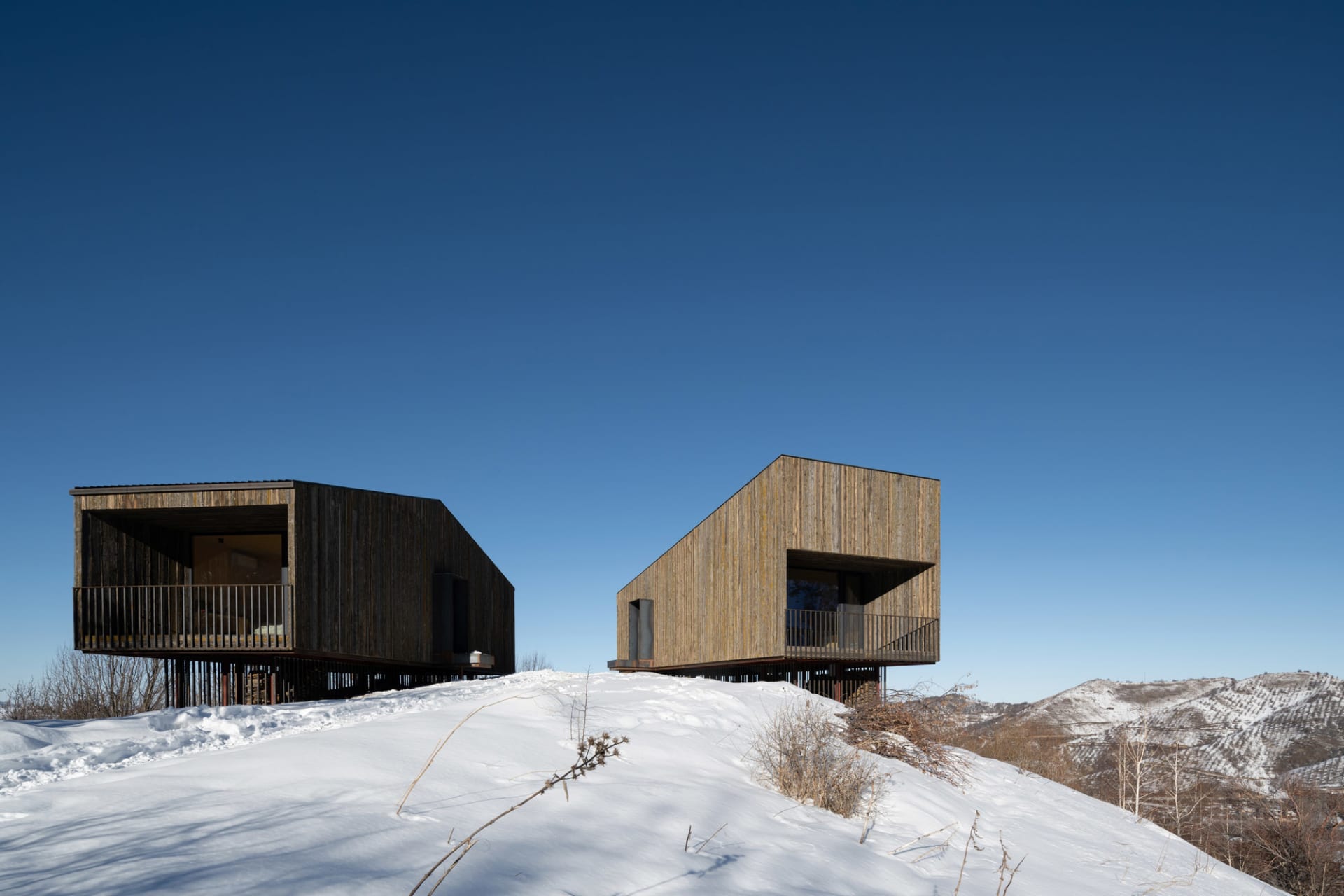 兩棟帶有木質包覆的現代住宅坐落於雪地山坡上