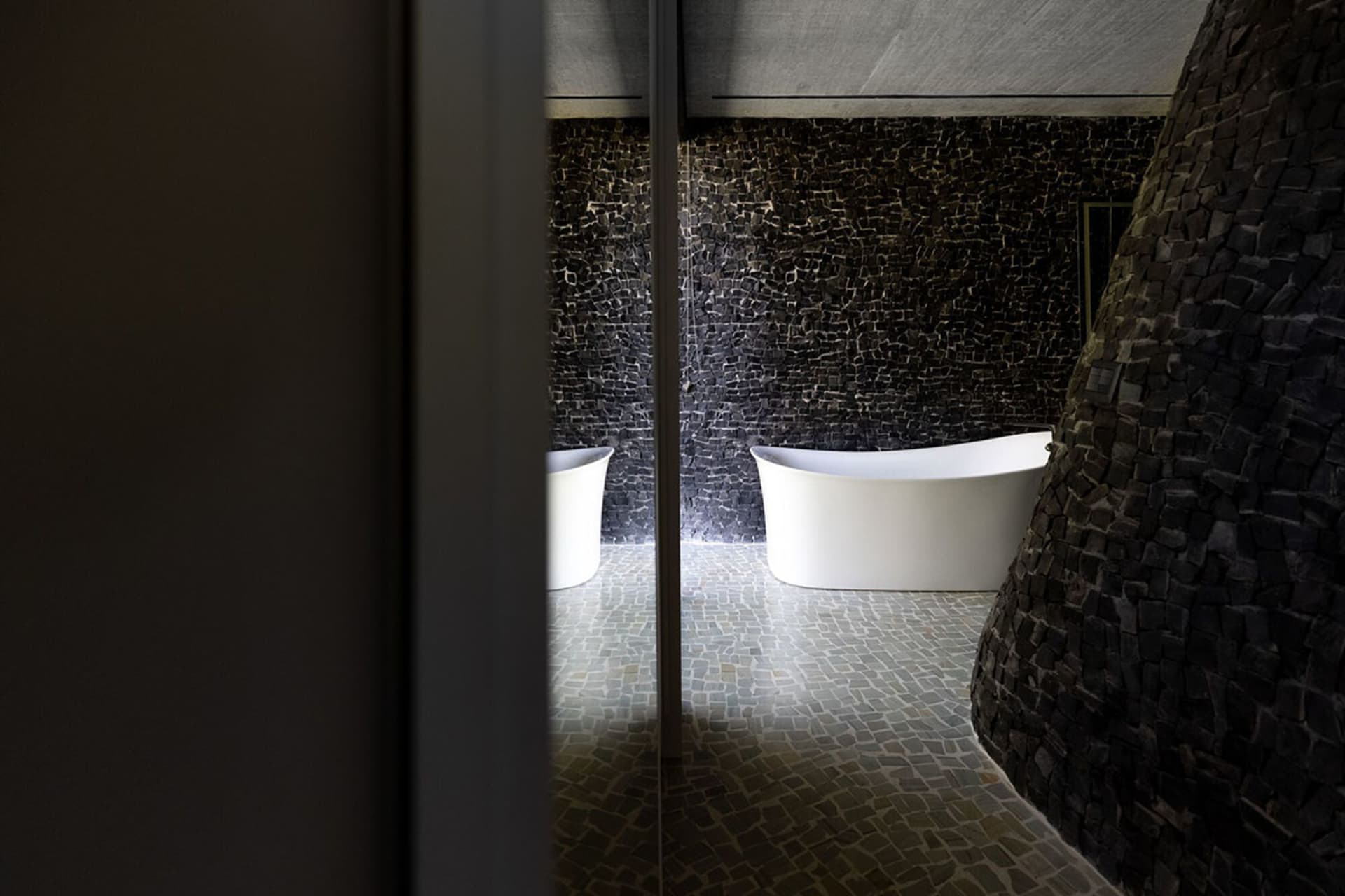 Modern bathroom interior with freestanding white bathtub against a black brick wall.