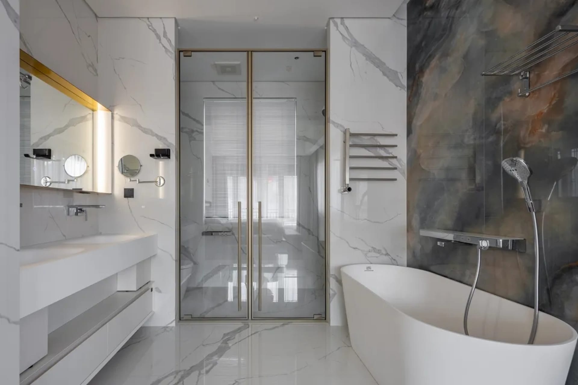 Modern bathroom with marble walls and floor, featuring a freestanding bathtub, a glass-enclosed shower, and a floating vanity