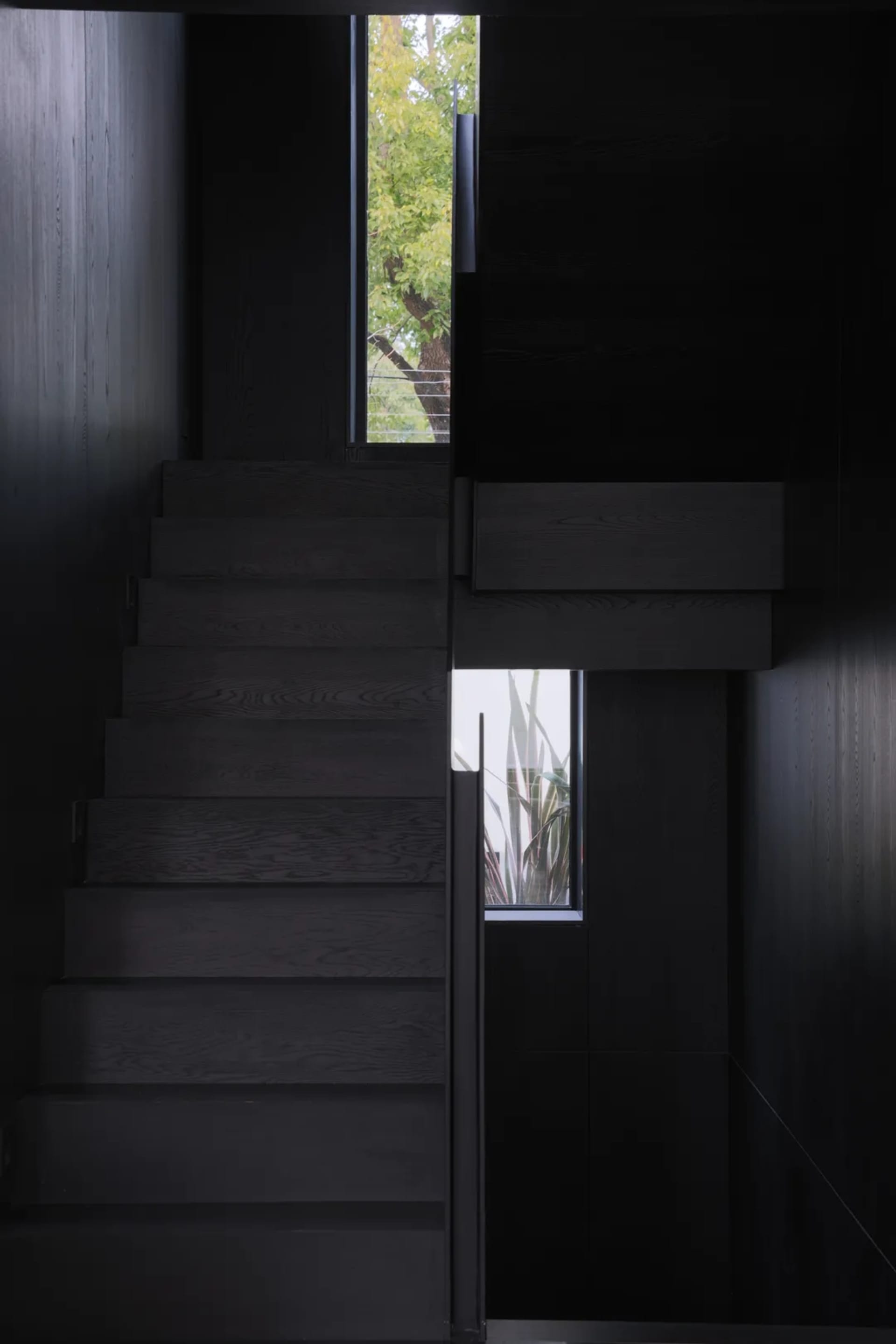 A modern black staircase with wooden steps in a dark interior space.