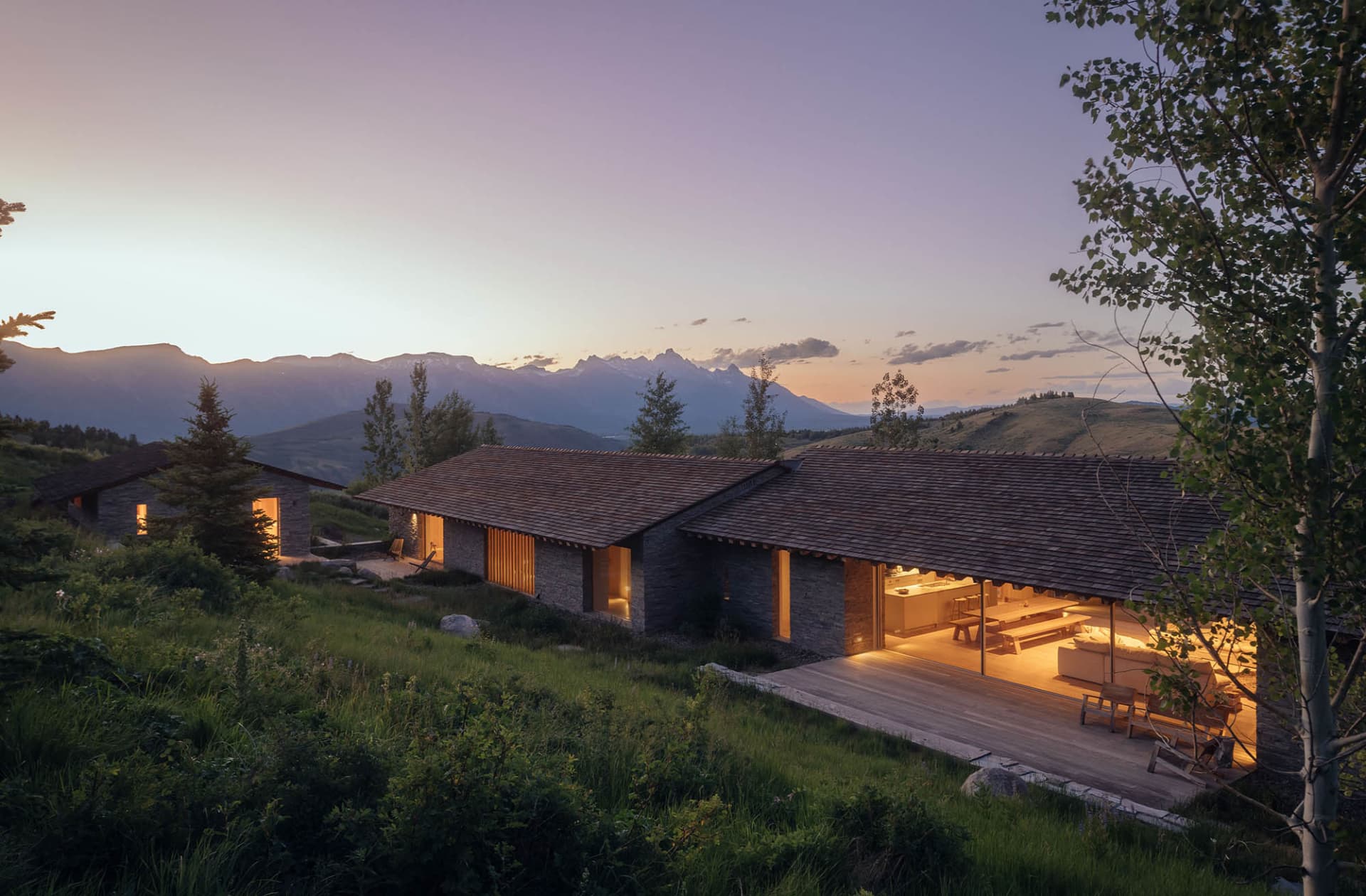 A modern residential exterior with stone walls and a wooden roof at dusk.