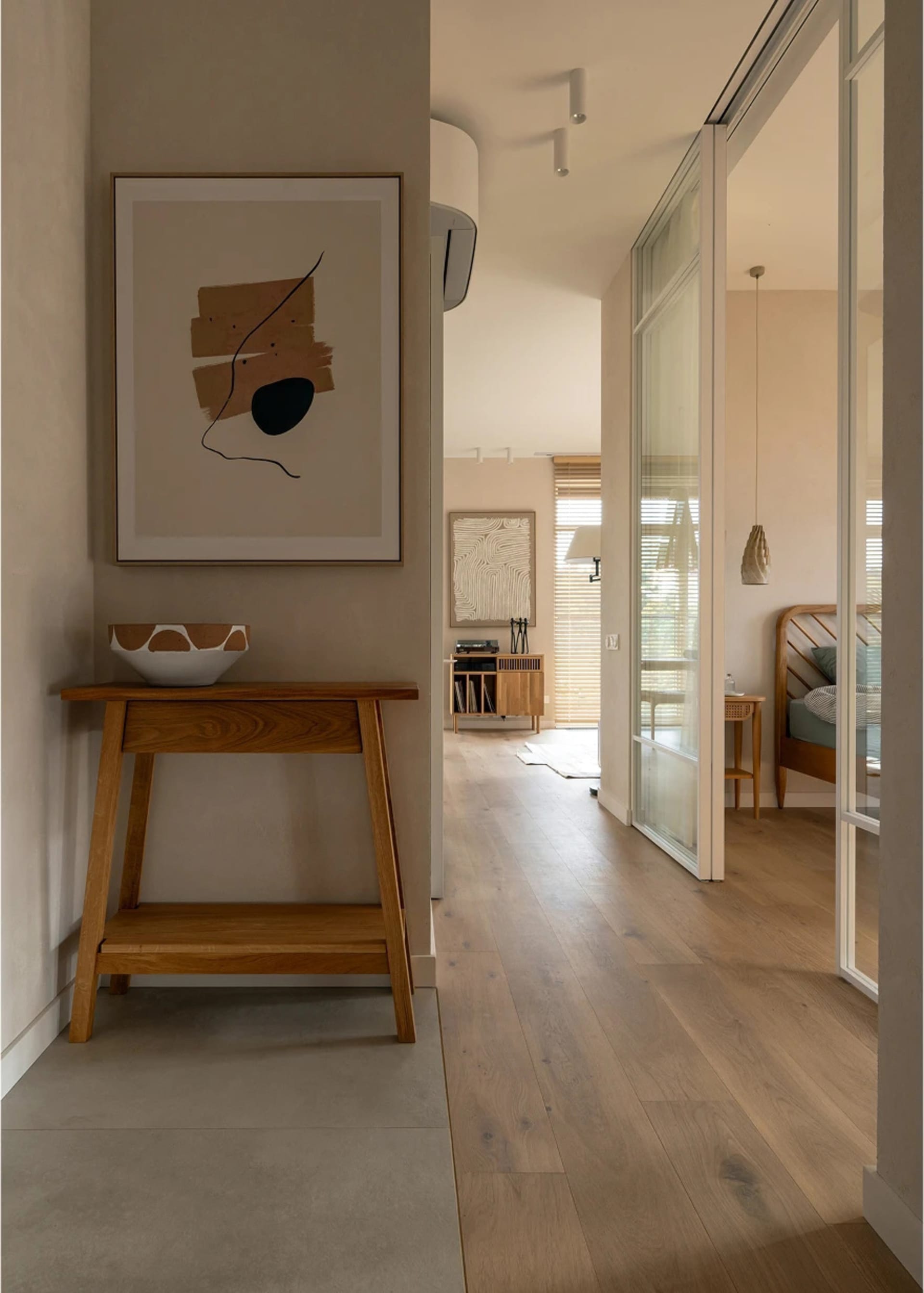Modern minimalist entryway featuring a wooden console table, abstract artwork, and wooden flooring.