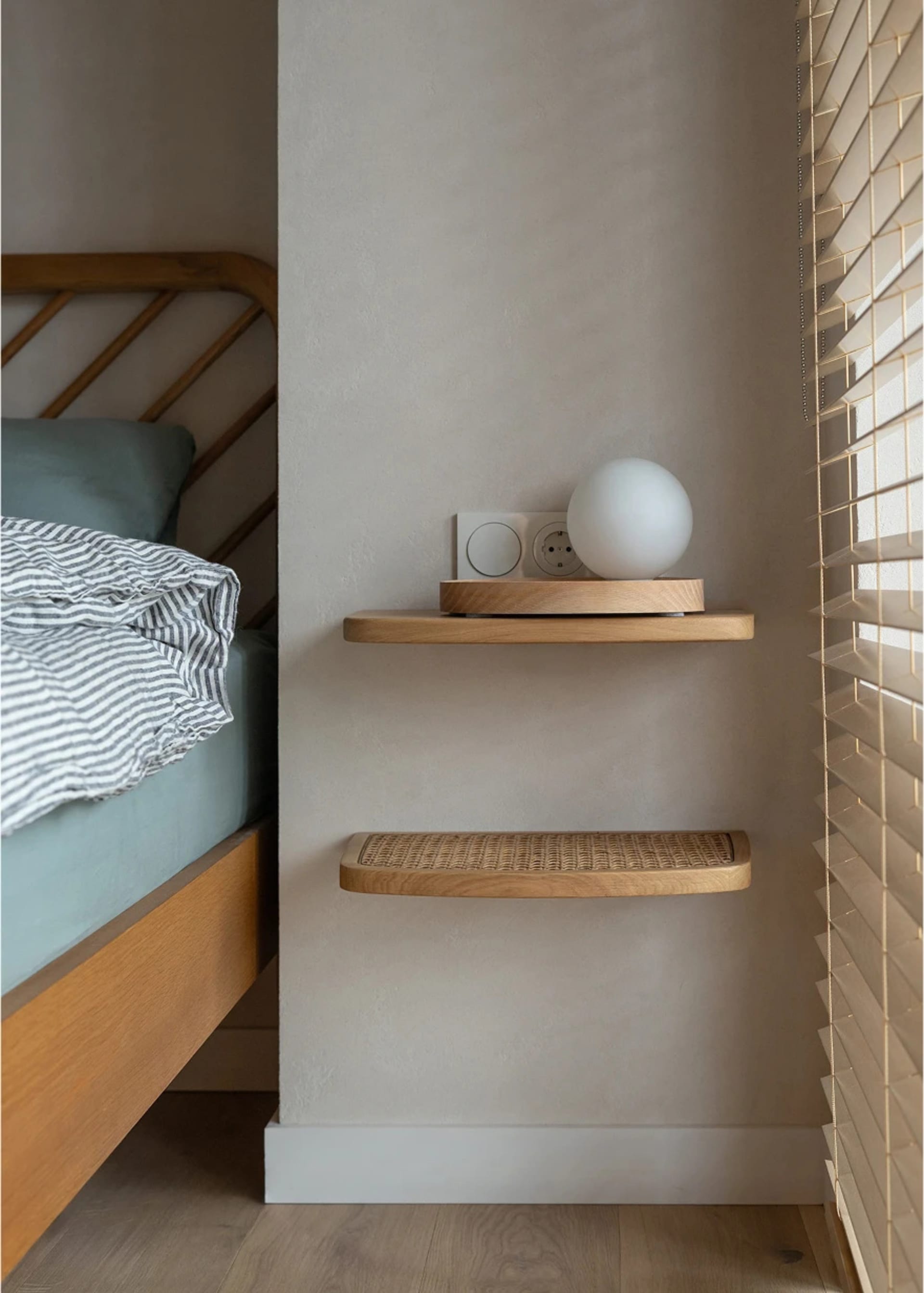 A minimalist bedroom featuring floating shelves made of wood, with a white spherical lamp, electrical outlets, and a bed with
