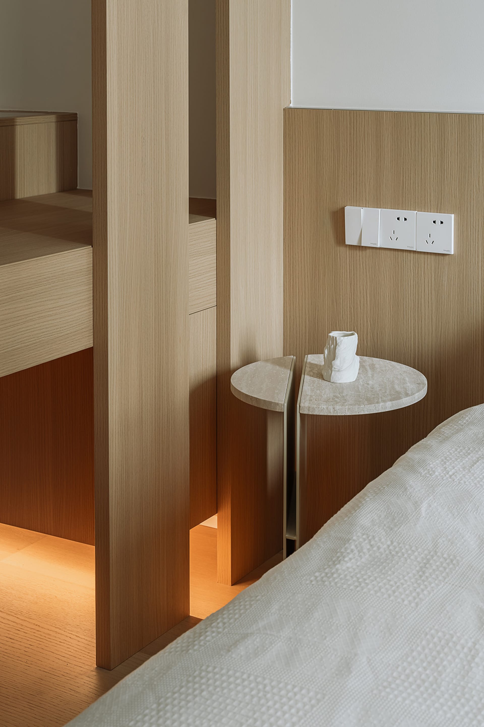 Bedroom with modern design and wooden furniture, including a round side table with a vase.