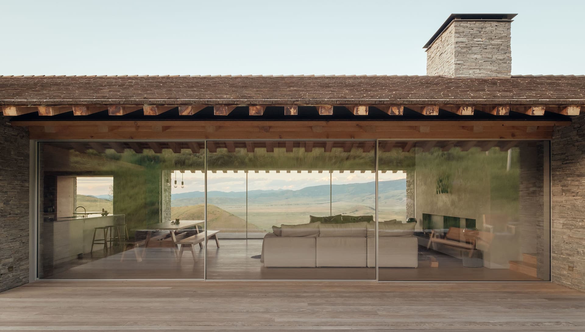 Modern rustic vacation home interior with wooden floor, stone wall, glass sliding doors, and scenic landscape view.