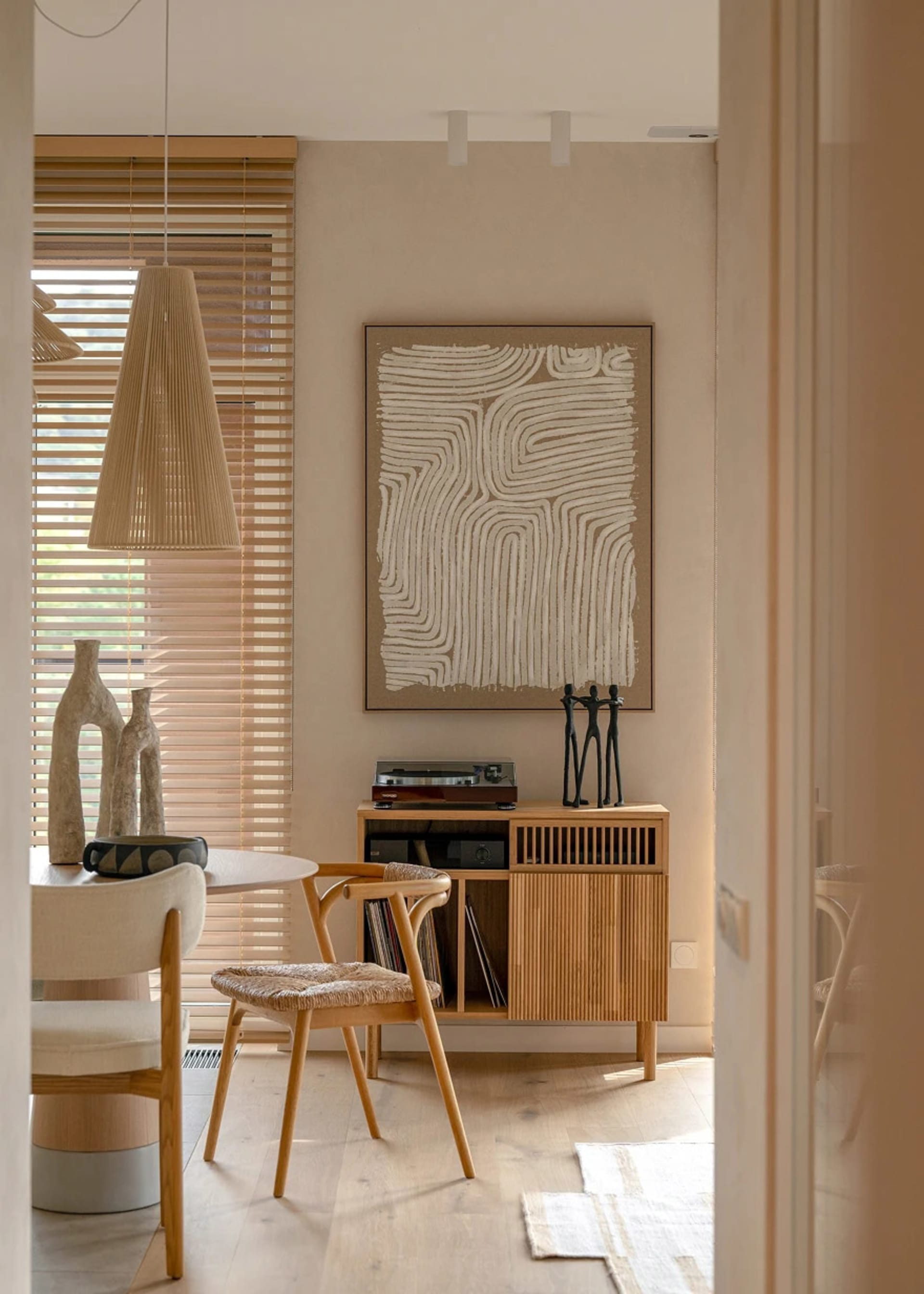 A minimalist living room featuring wooden furniture, a pendant light, and abstract wall art.