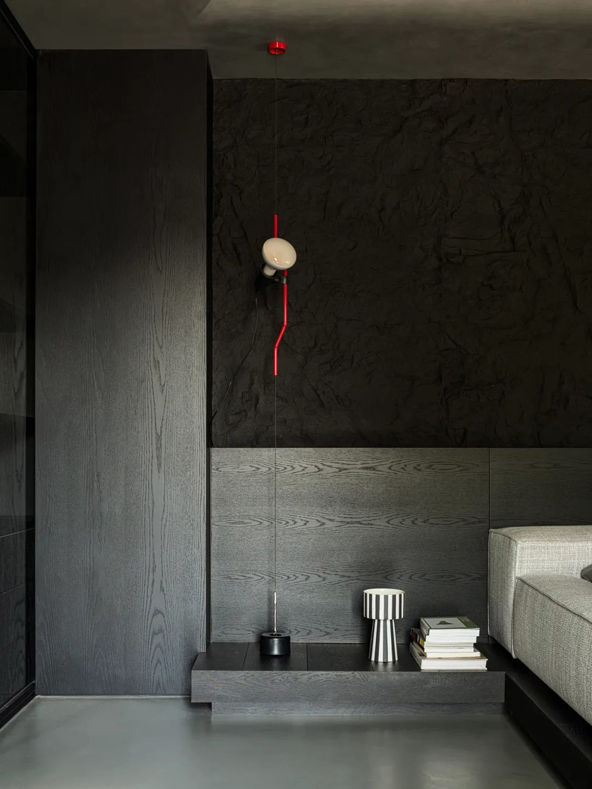 A minimalist living room featuring dark wood walls, concrete flooring, and a gray sofa.