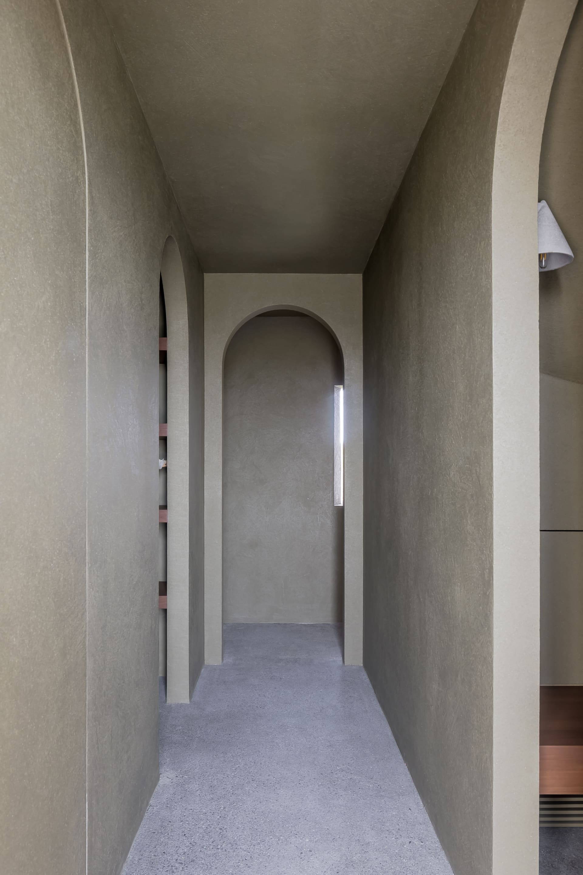 Modern interior space featuring a minimalist design with concrete walls and a long hallway with arches and a skylight.
