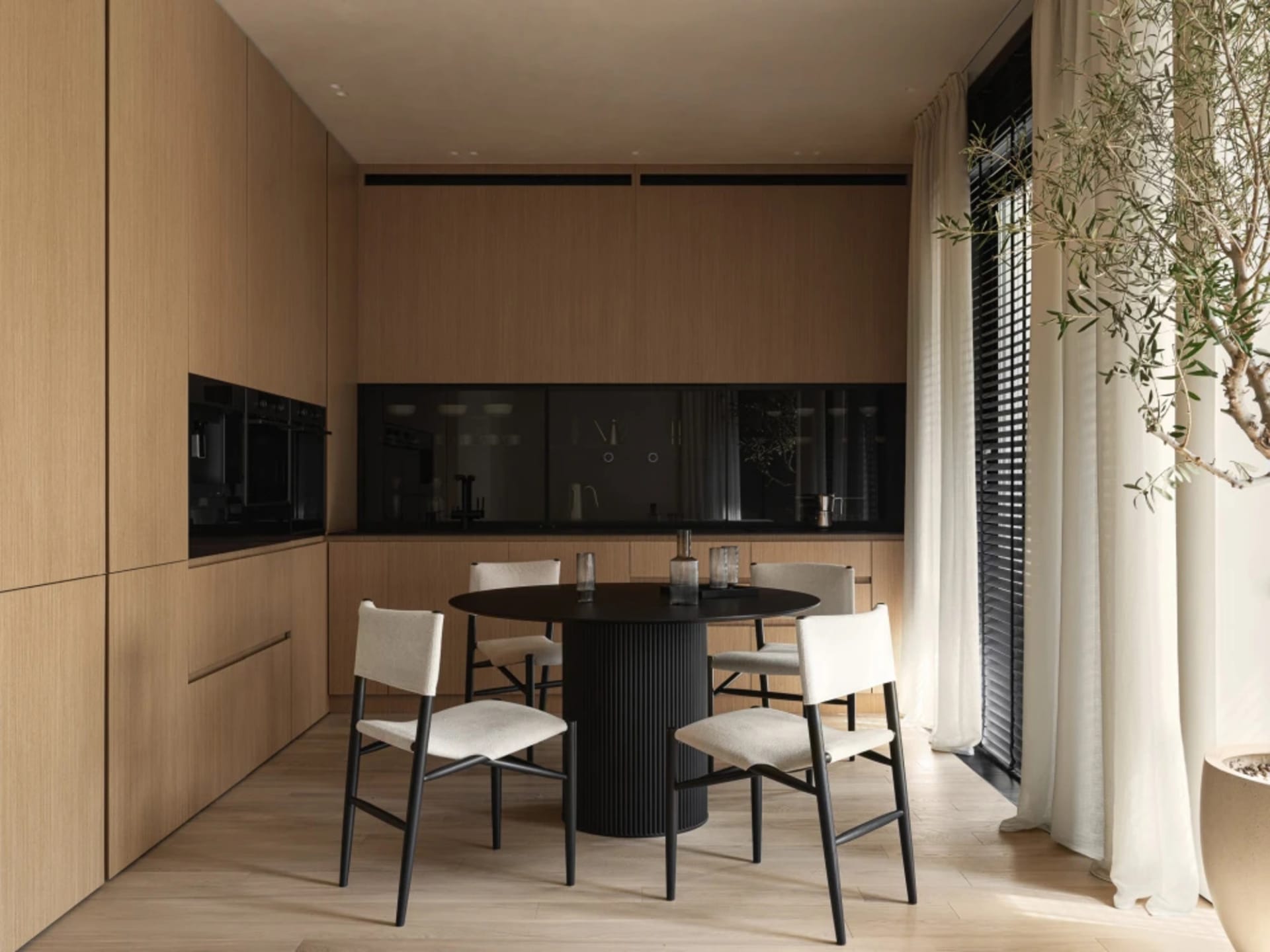 A modern residential kitchen featuring wooden cabinets, a black dining table, and white upholstered chairs.