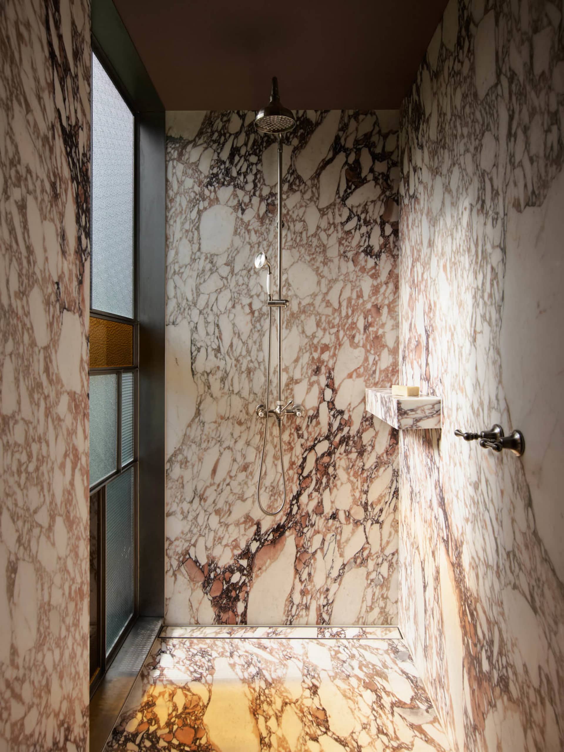 Modern minimalist bathroom with marble walls, shower, and a window.